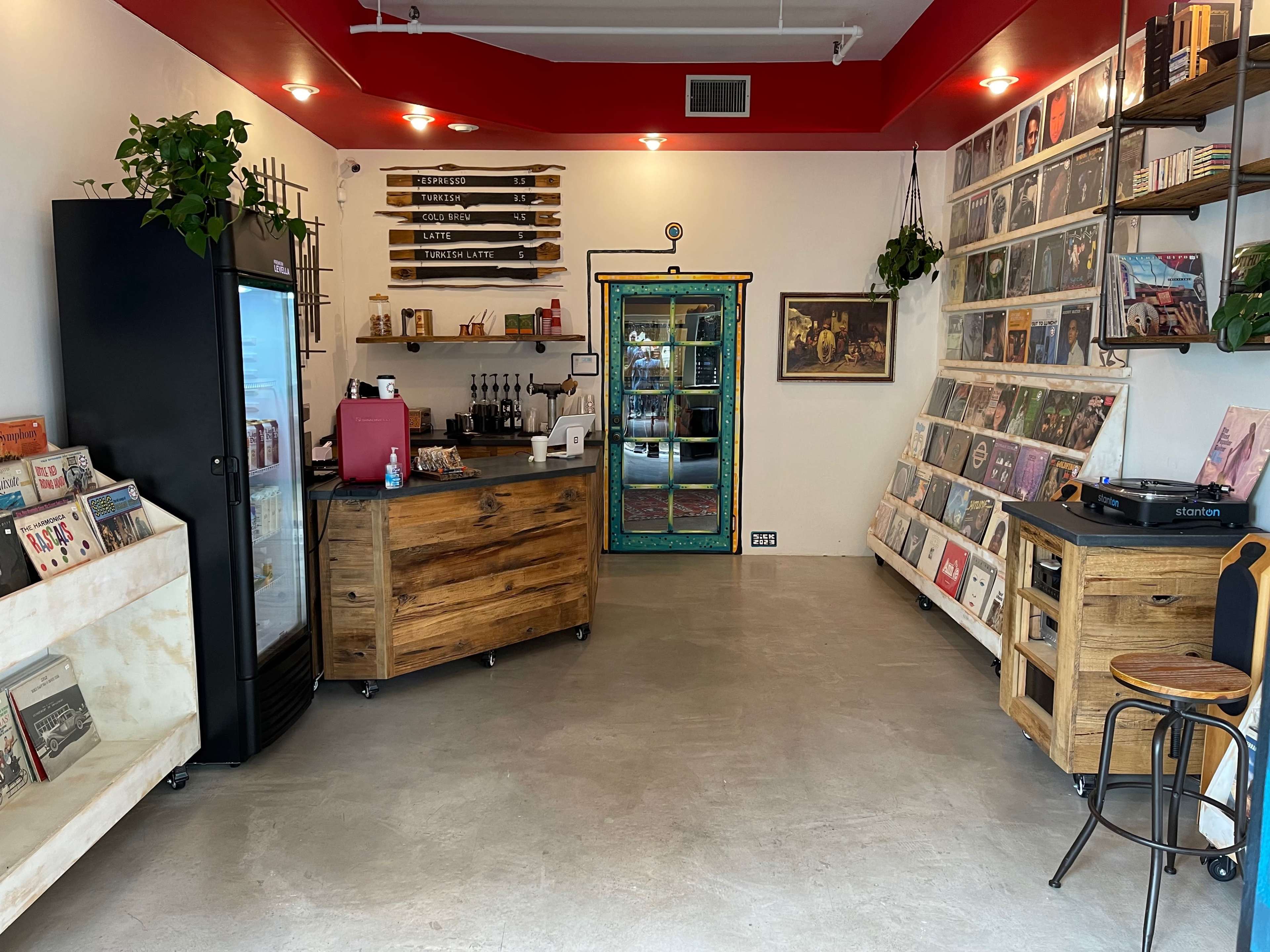A modern café and record shop with wooden furniture, a refrigerator, and walls adorned with vinyl records and plants.