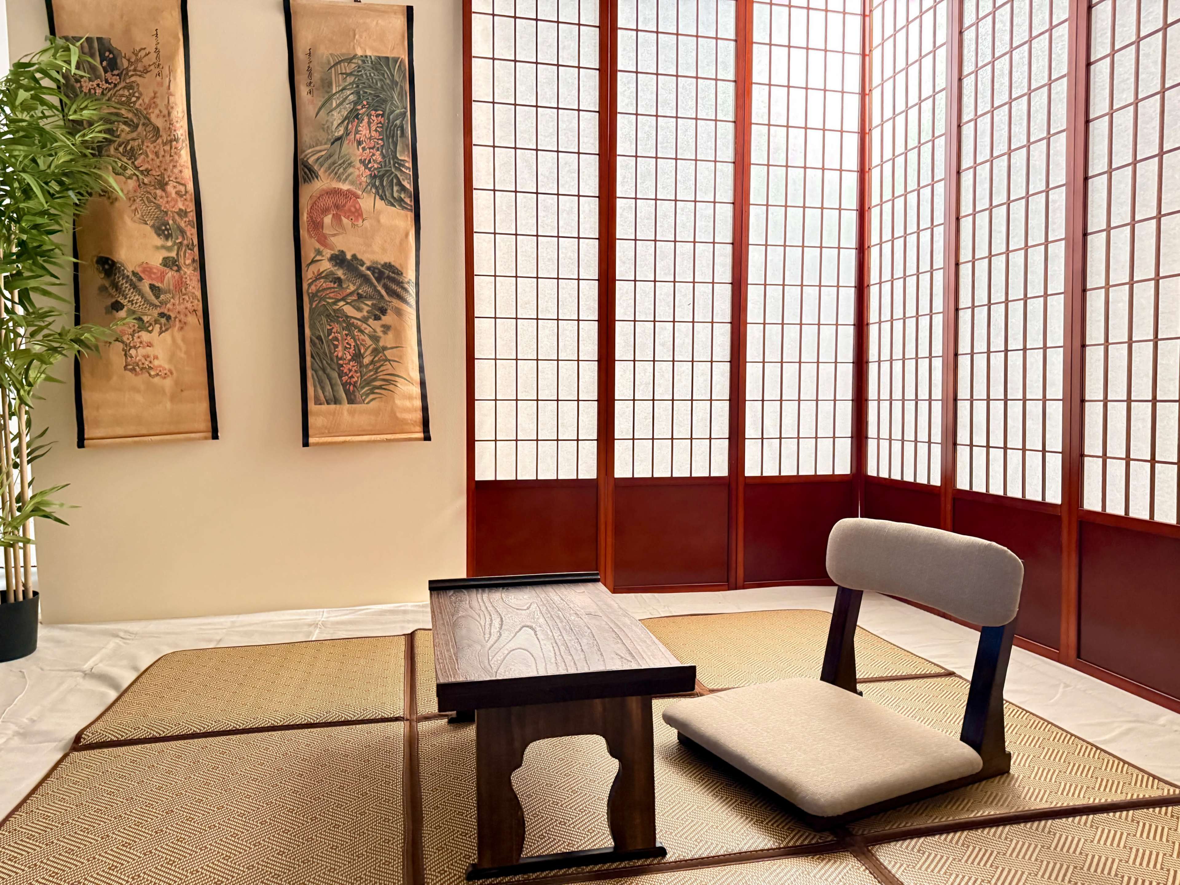 The image shows a minimalist Japanese-style room with tatami flooring, alow table, a single chair, and decorative wall scrolls.