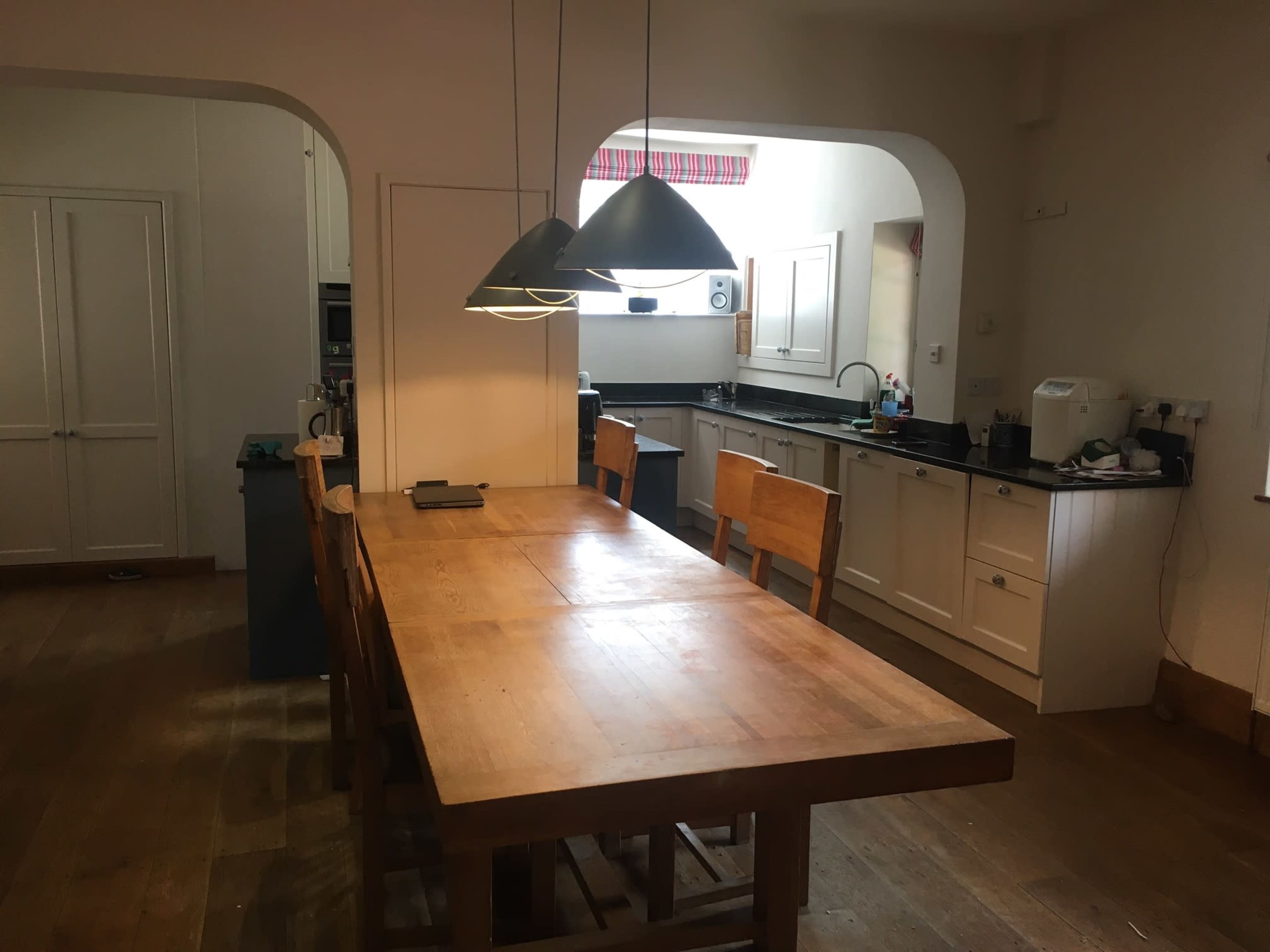 A modern kitchen with white cabinets, a large wooden dining table, and pendant lights hanging above it.