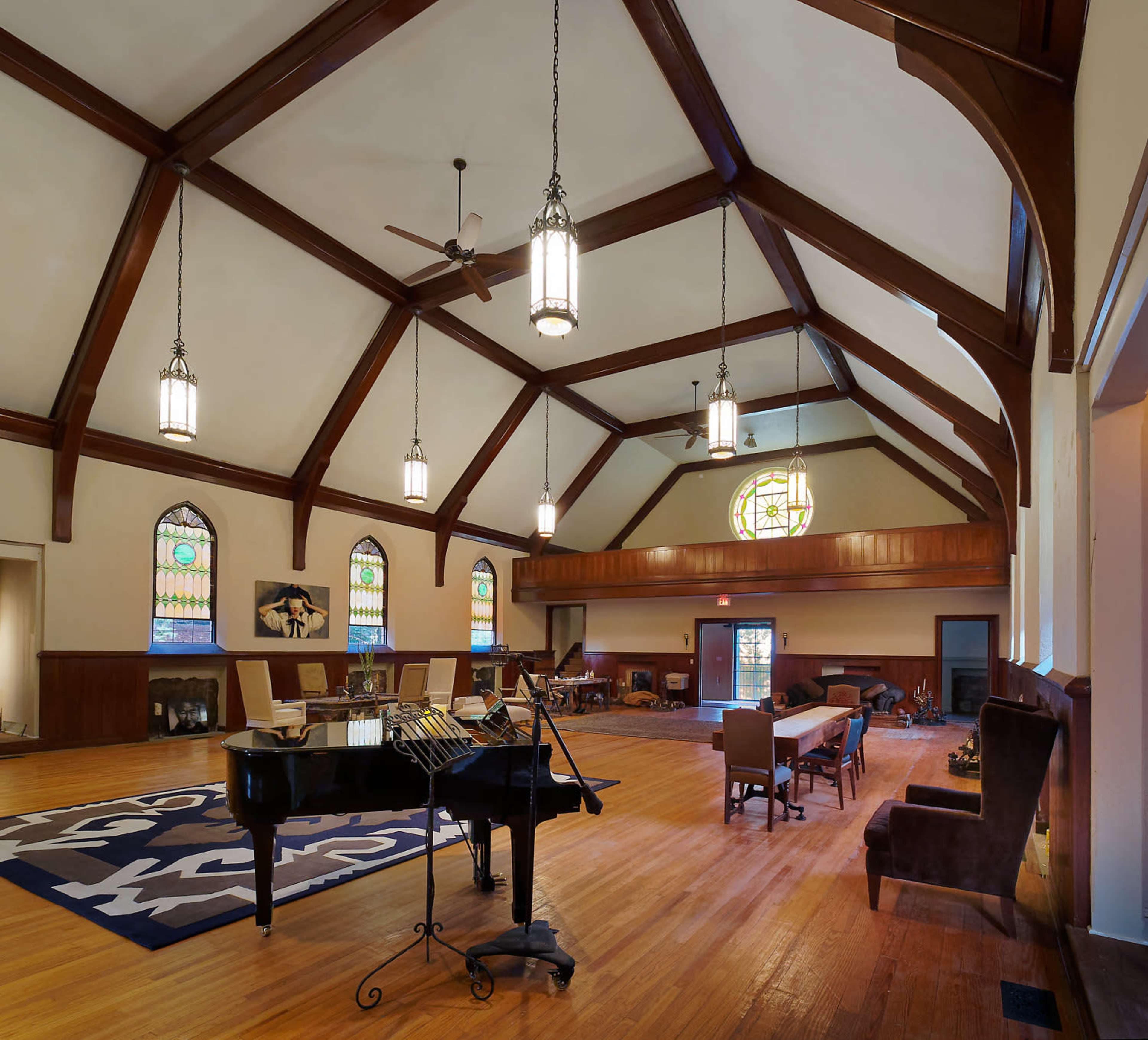 A spacious interior of a hall with a vaulted ceiling, wooden beams, and a grand piano in the foreground, alongside tables and chairs arranged for gatherings.