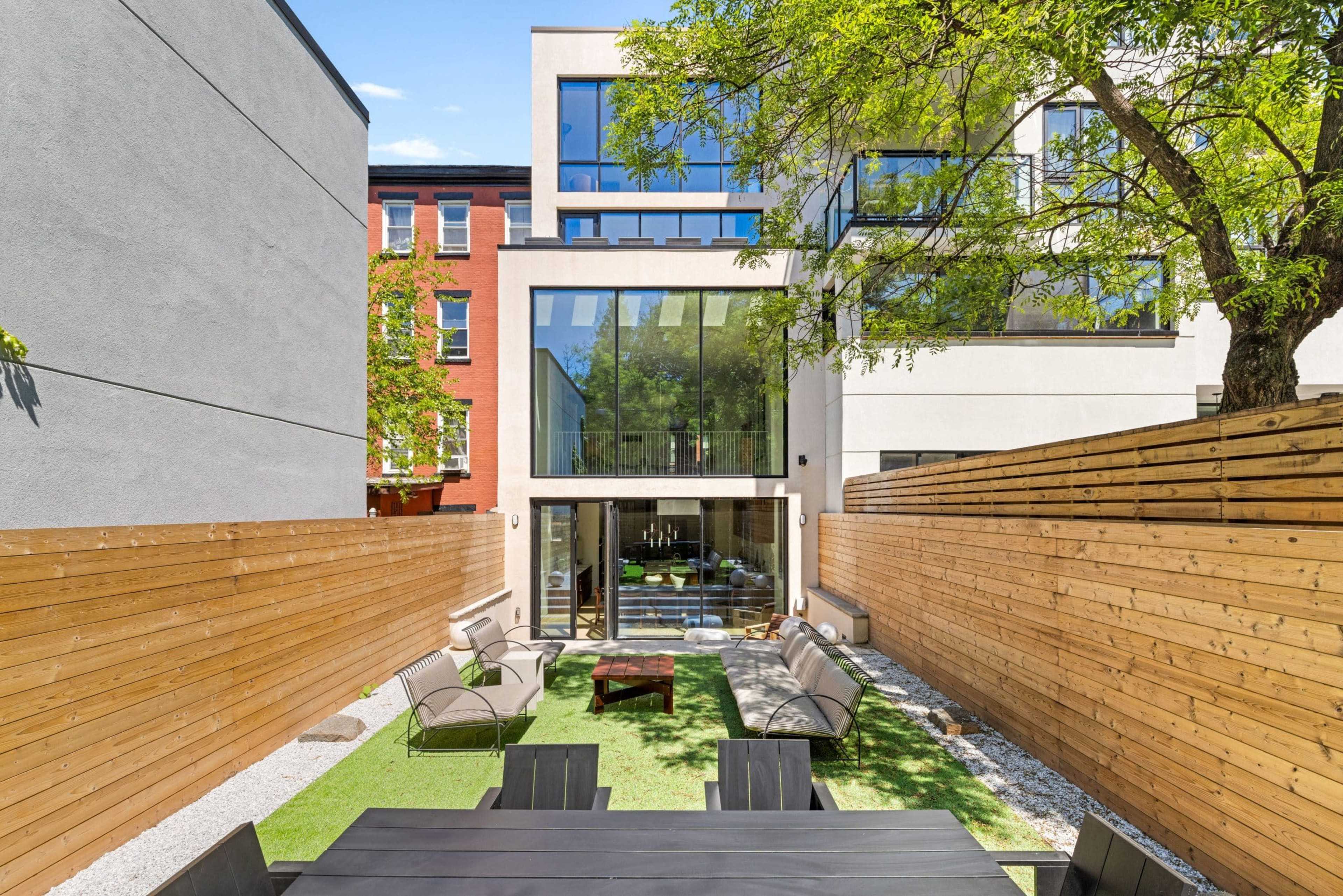A modern courtyard features a glass wall view of a contemporary building, surrounded by wooden fences and equipped with seating and greenery.