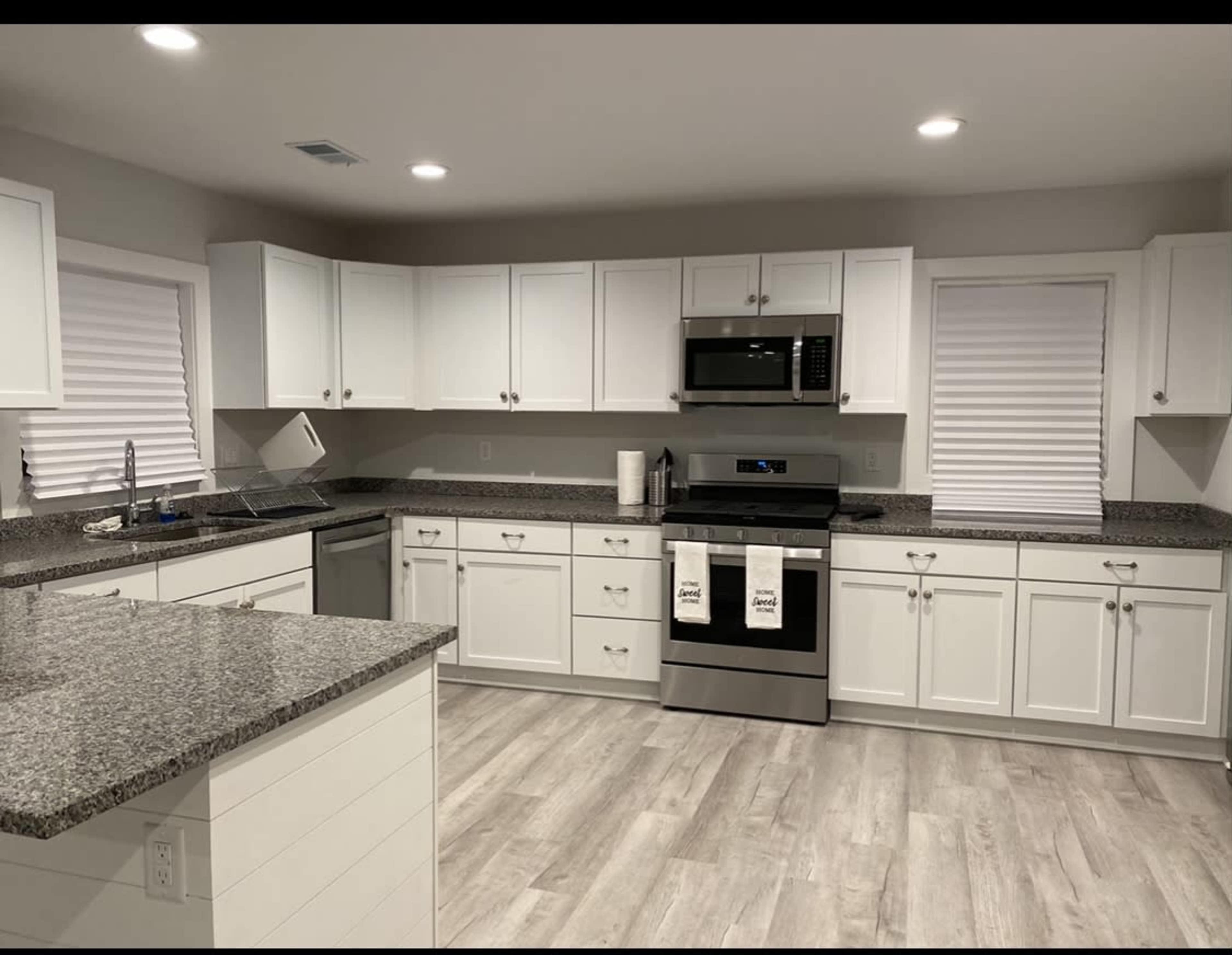 A modern kitchen features white cabinetry, stainless steel appliances, and a granite countertop with a light wood floor.