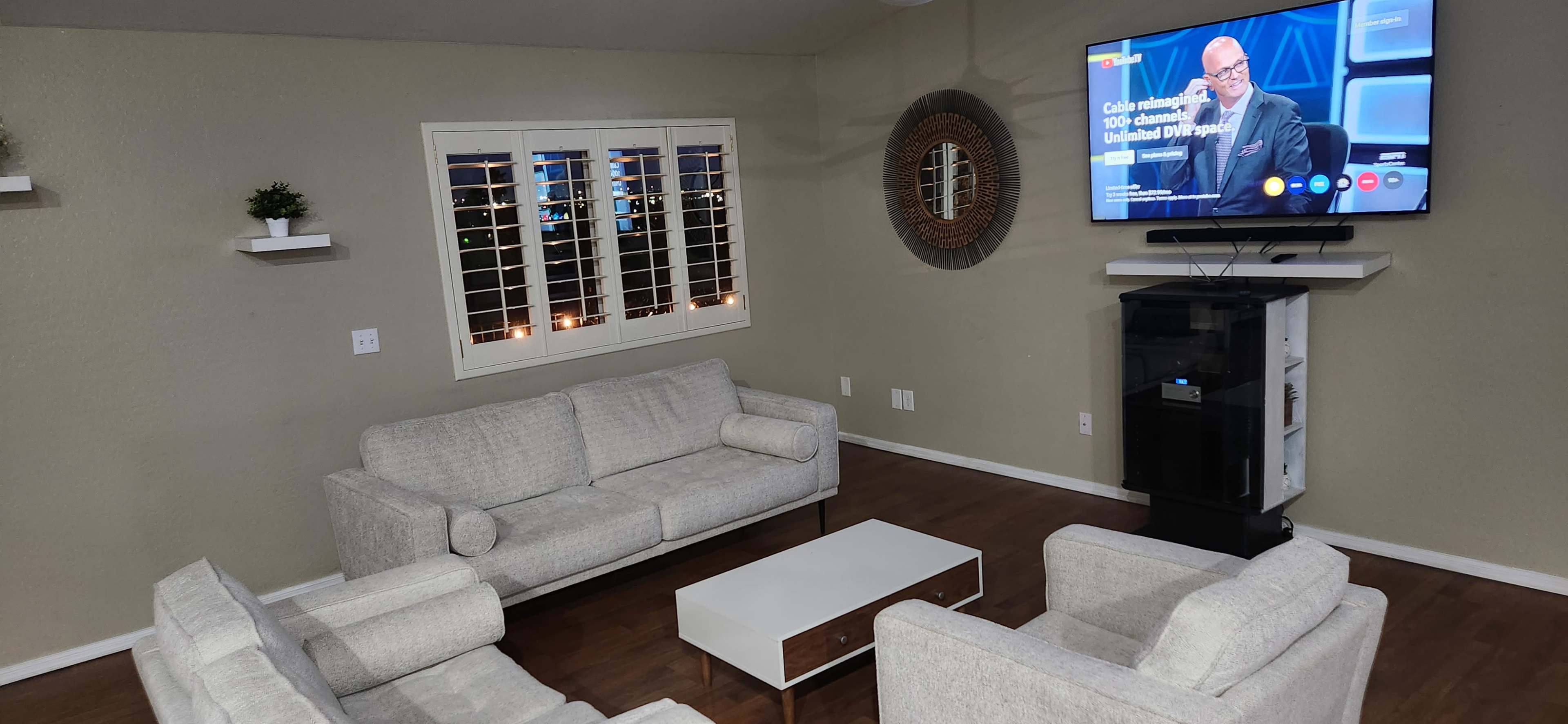 A living room with two light gray sofas, a white coffee table, and a TV mounted on the wall displaying a news program.