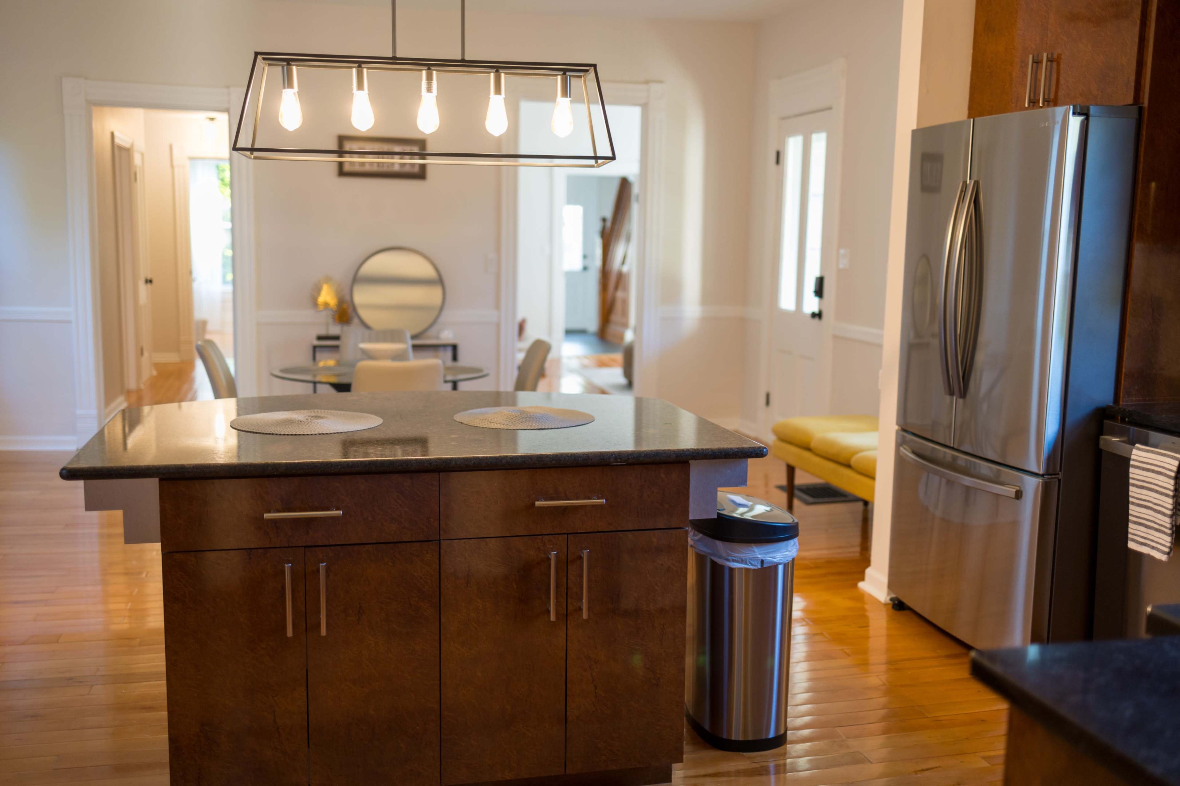The image shows a modern kitchen with a central island, pendant lighting, and stainless steel appliances.
