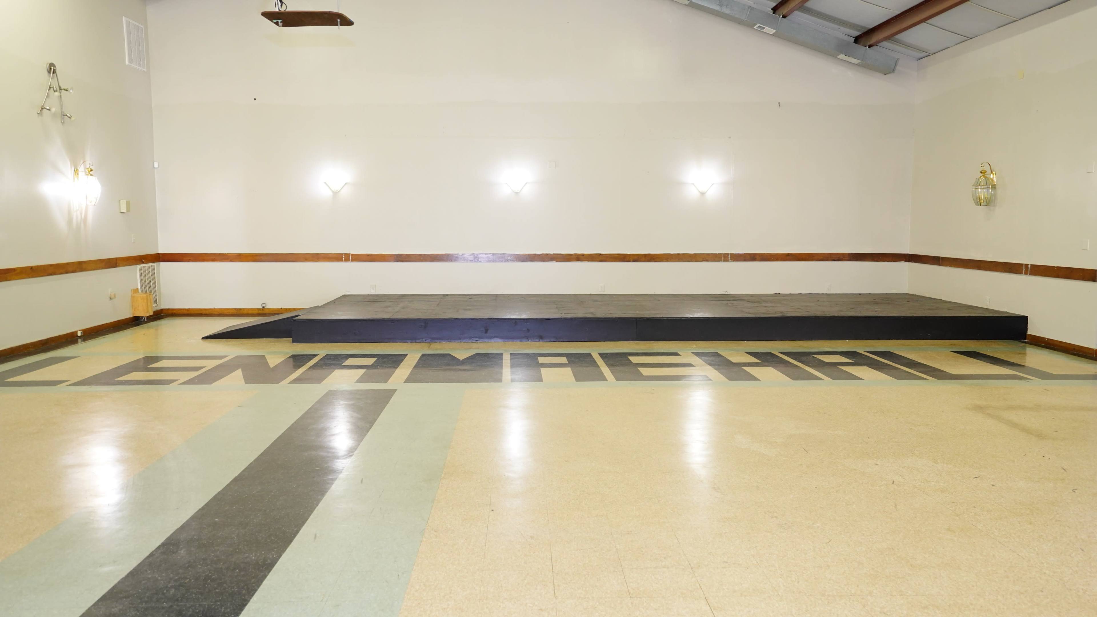 A dance hall with a dark stage at one end and the word "LENAMAHA" displayed on the floor in large letters.