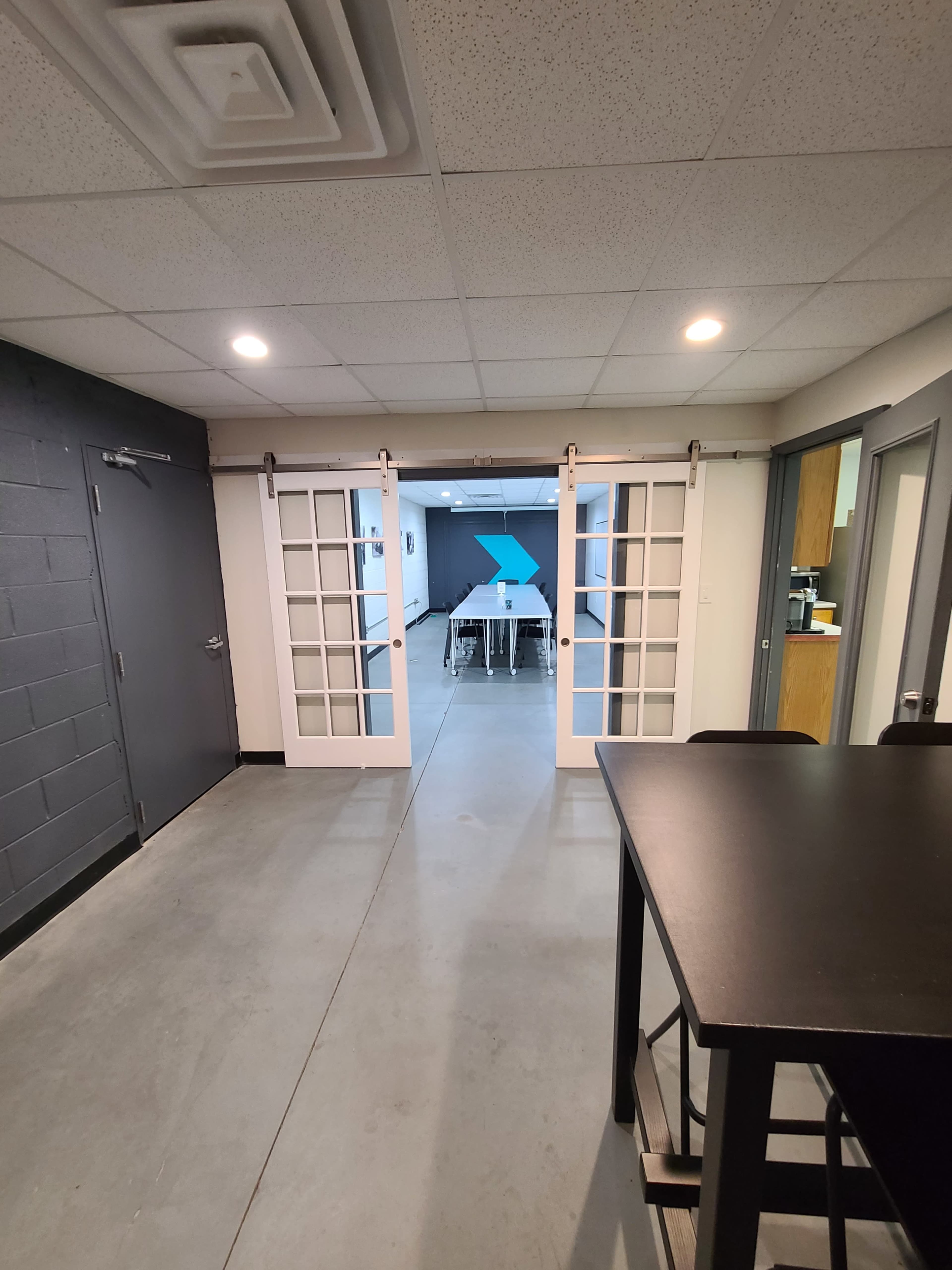 A hallway leading to a room with a table, framed by a set of sliding glass doors and a dark wall on the left.