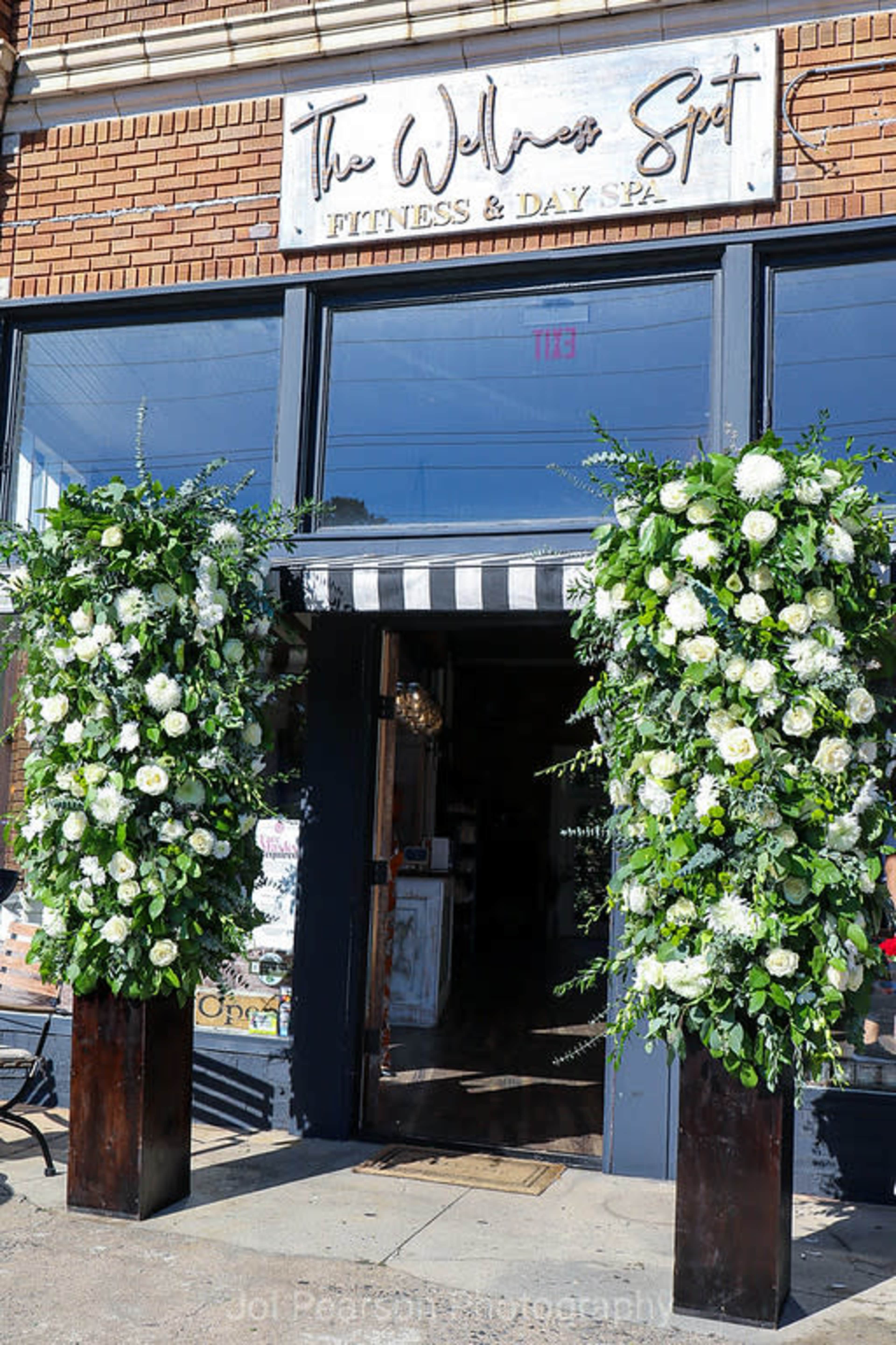 The entrance of a fitness and day spa features two tall flower arrangements on either side of the doorway.