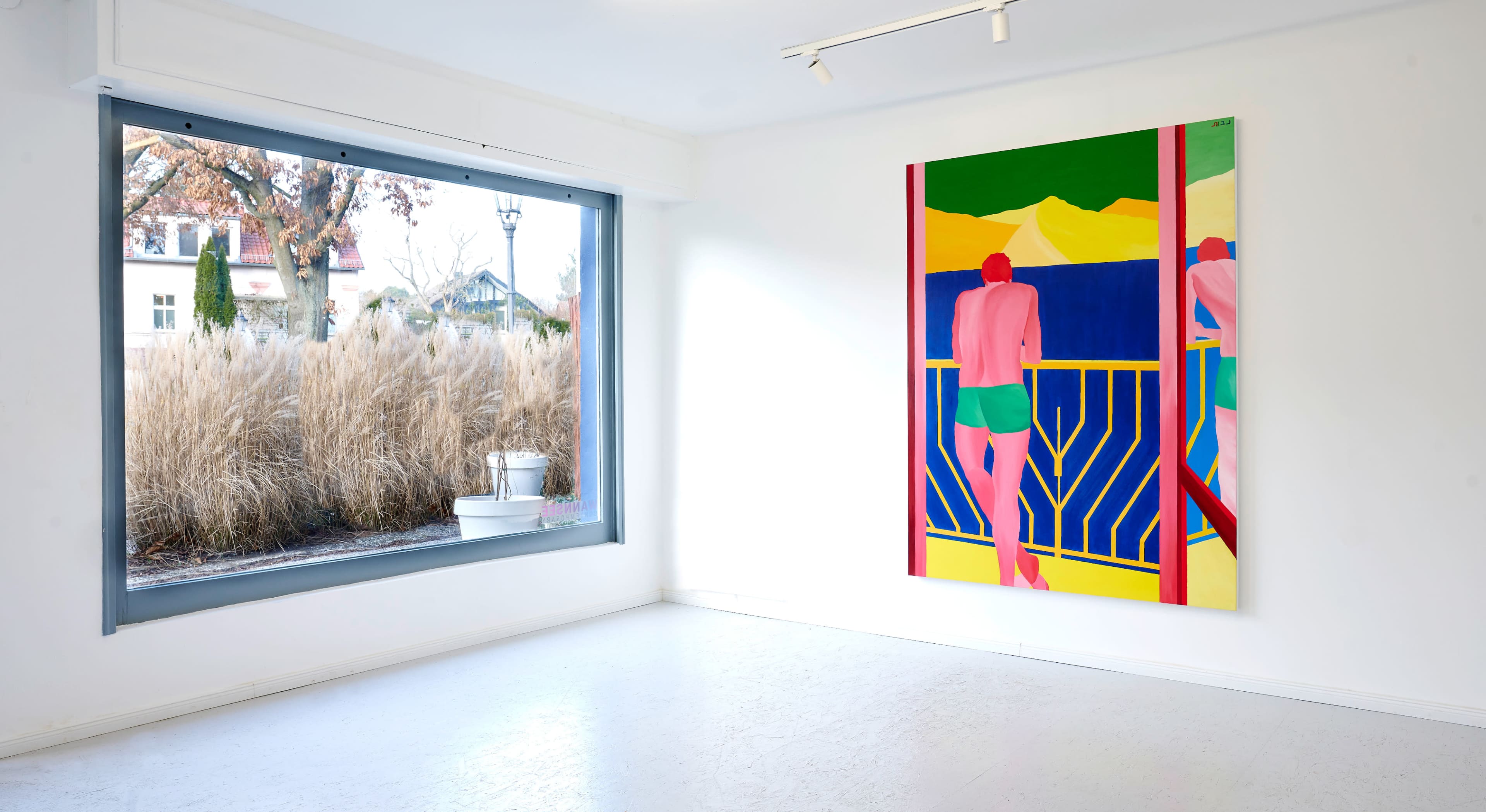 A brightly colored painting of a figure stands on the wall of a minimalist gallery with a large window overlooking tall grass outside.