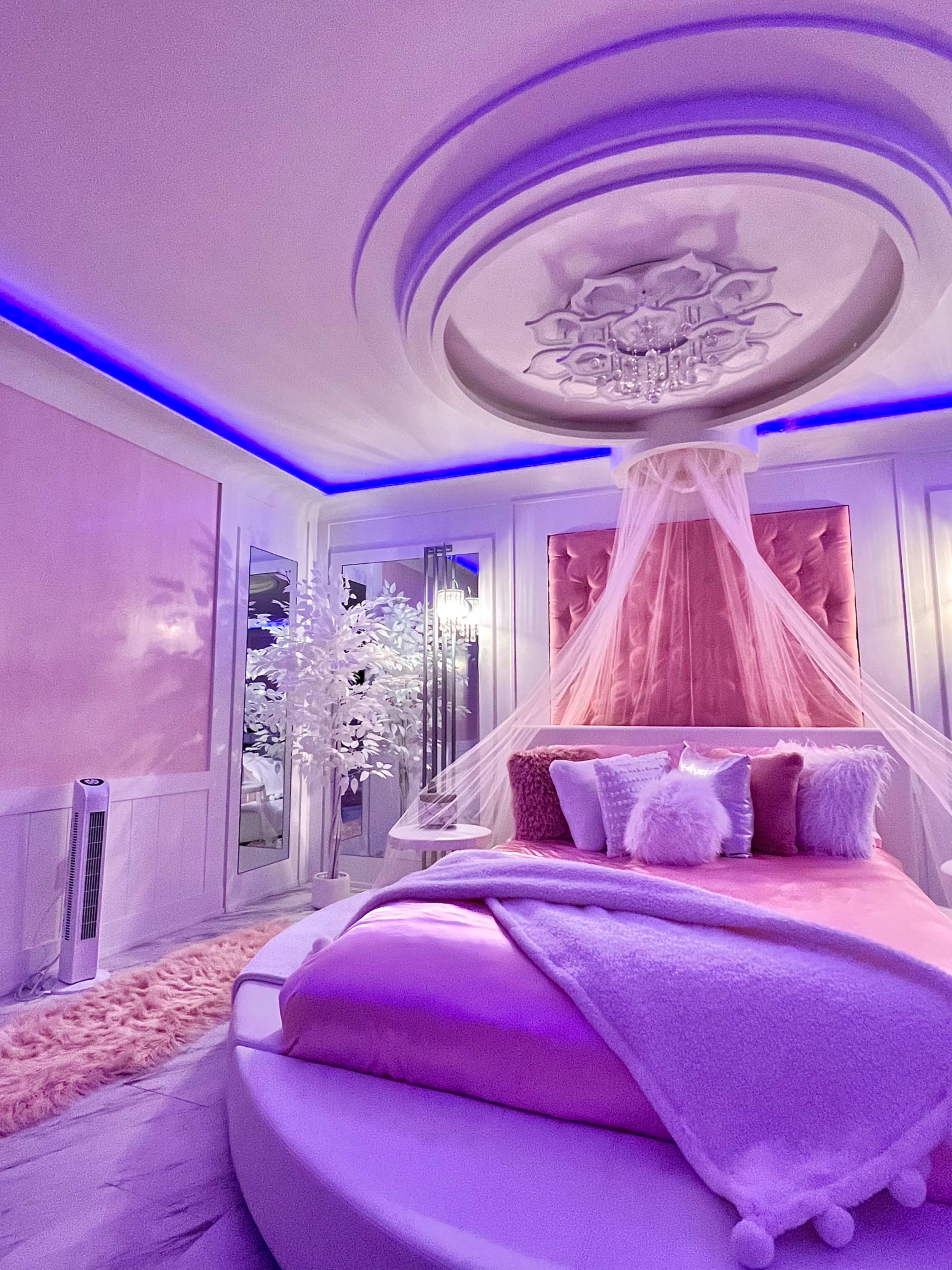 The room features a round bed adorned with pink bedding and pillows, a softly illuminated ceiling, and a decorative tree.