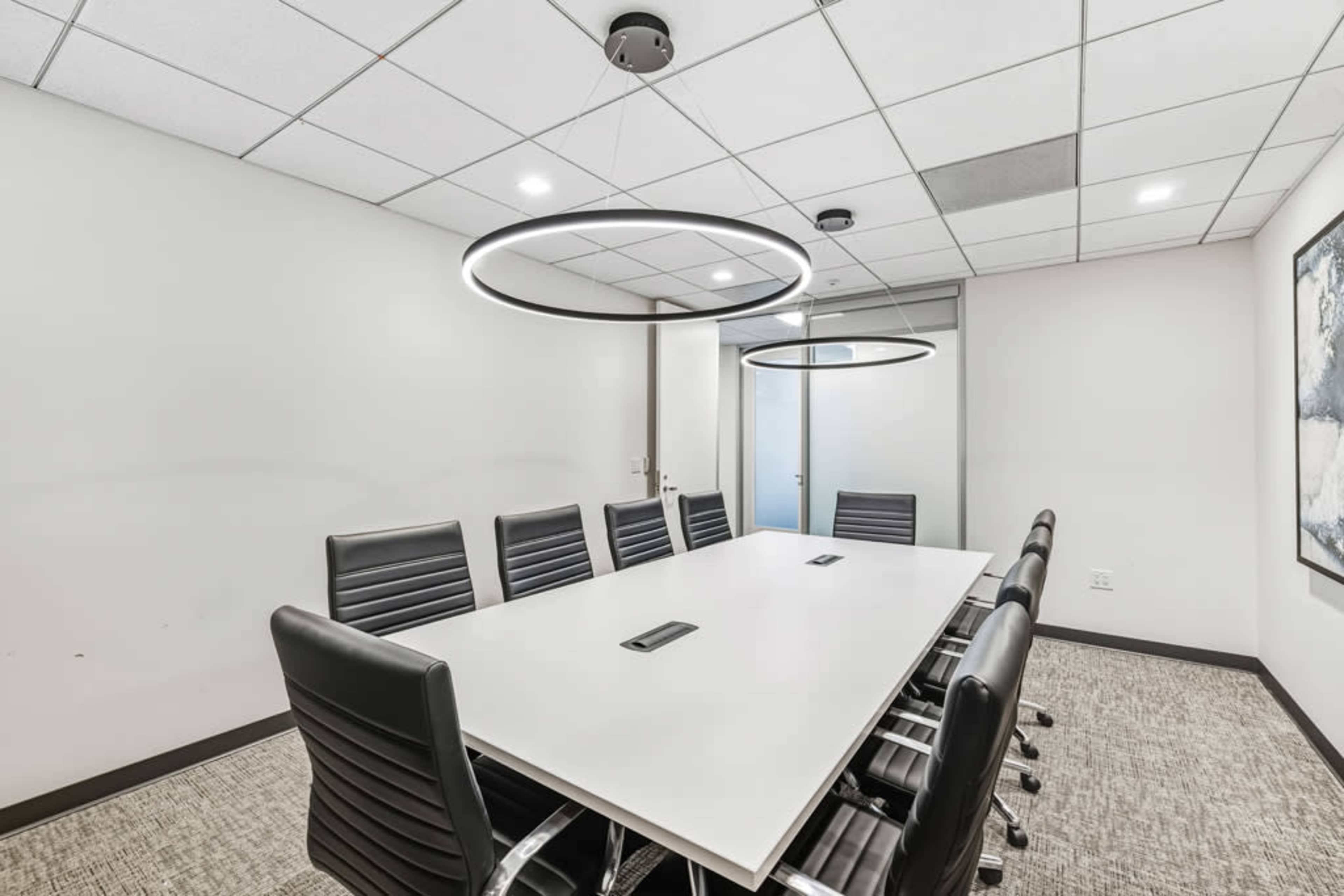 The image shows a modern conference room with a large white table surrounded by black leather chairs and two circular pendant lights hanging above.