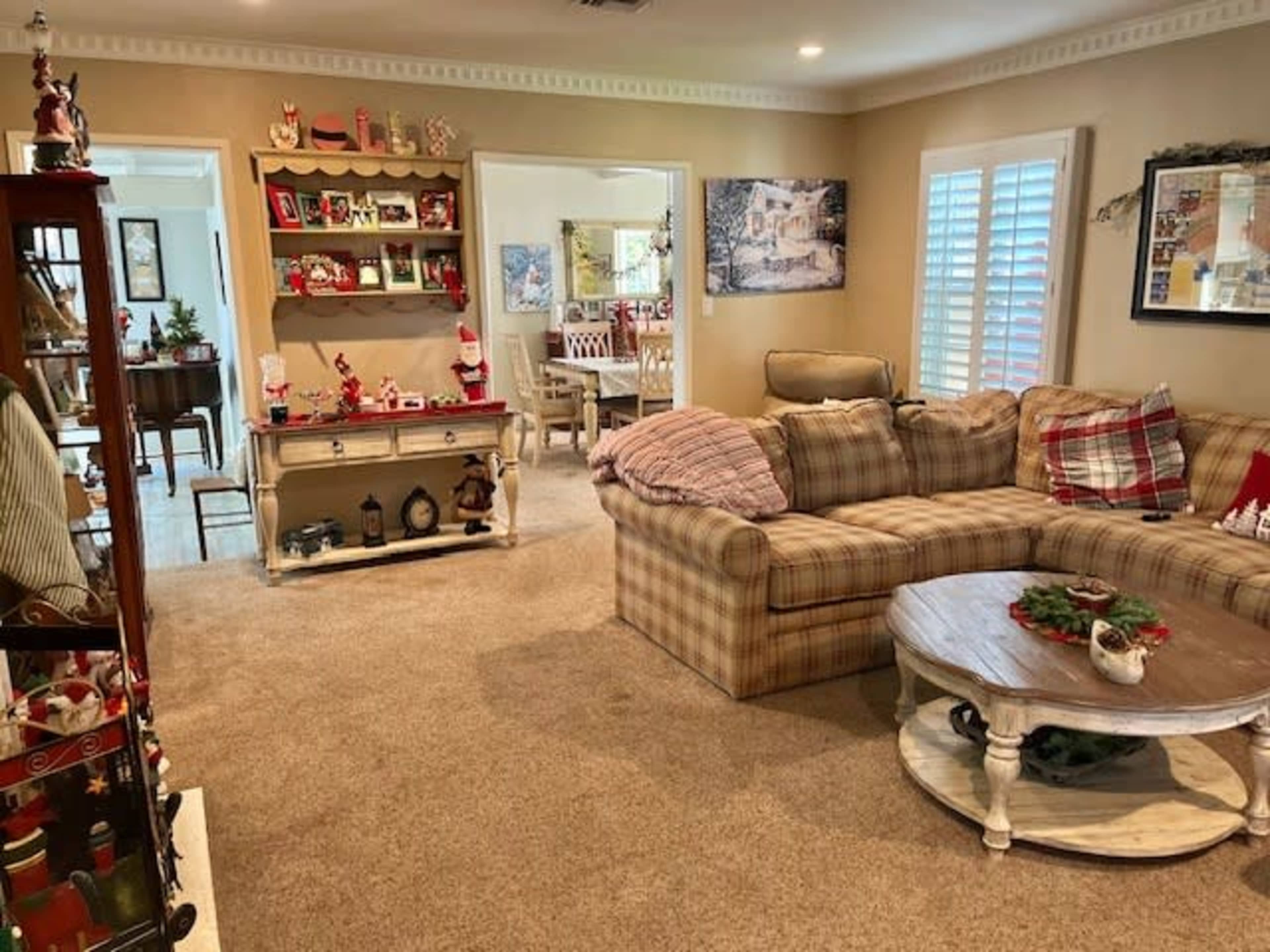 A cozy living room decorated for the holiday season, featuring a large sectional sofa, a wooden coffee table, and various festive decorations on the shelves and tables.