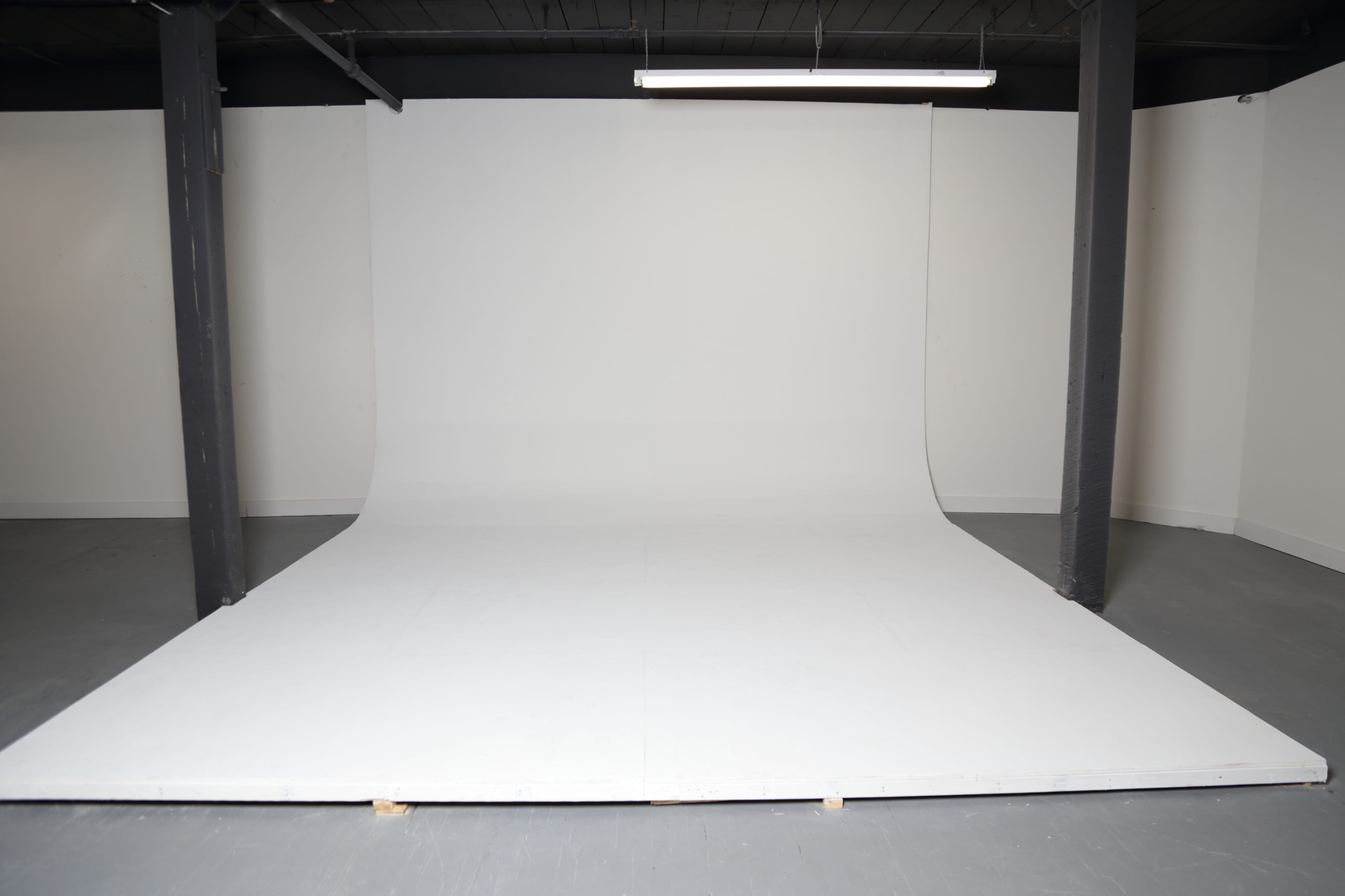 A spacious photography studio with a seamless white backdrop and a gray floor.