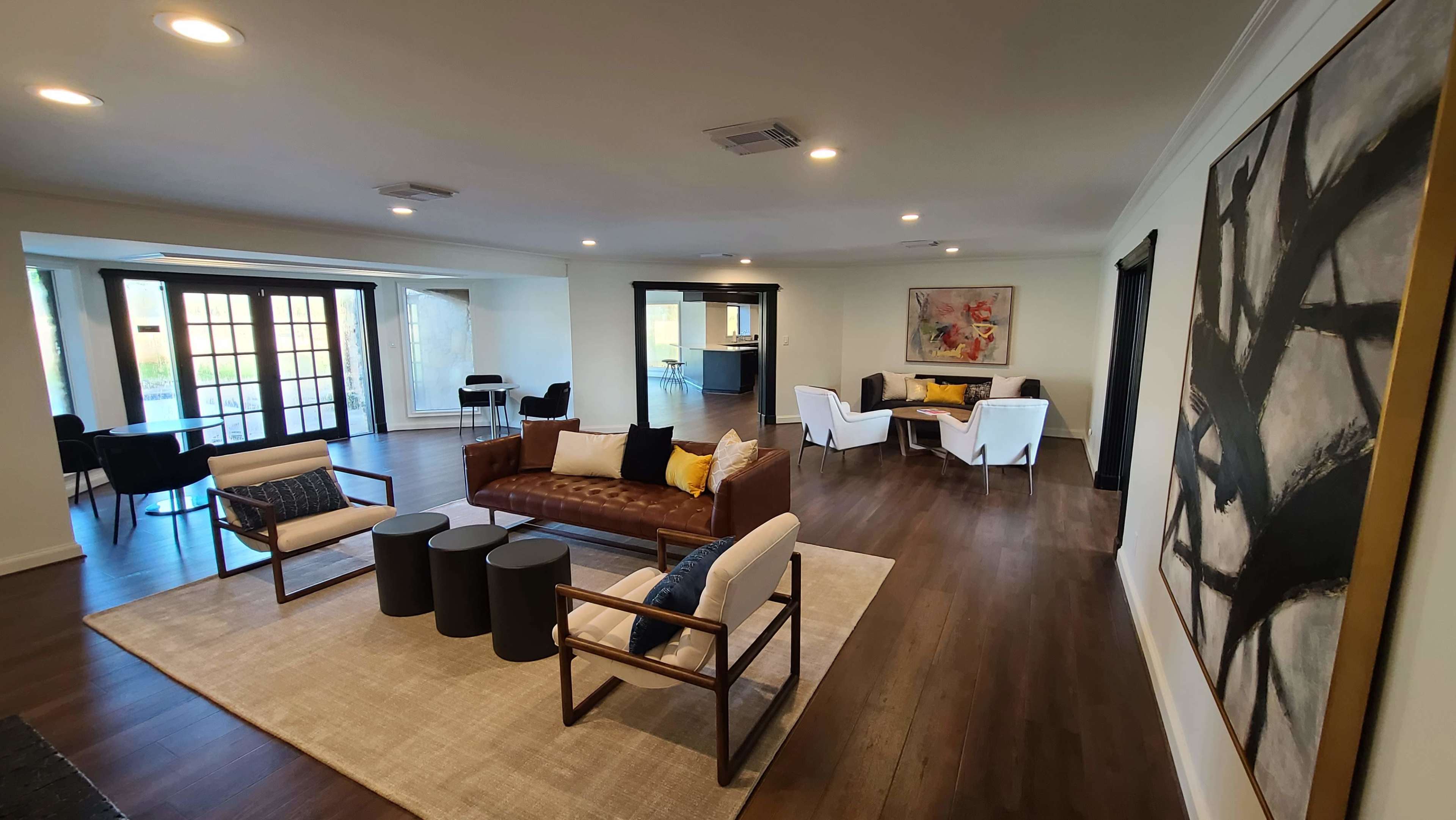 The image shows a spacious, modern living area with a seating arrangement, a dining area, and large windows allowing natural light.