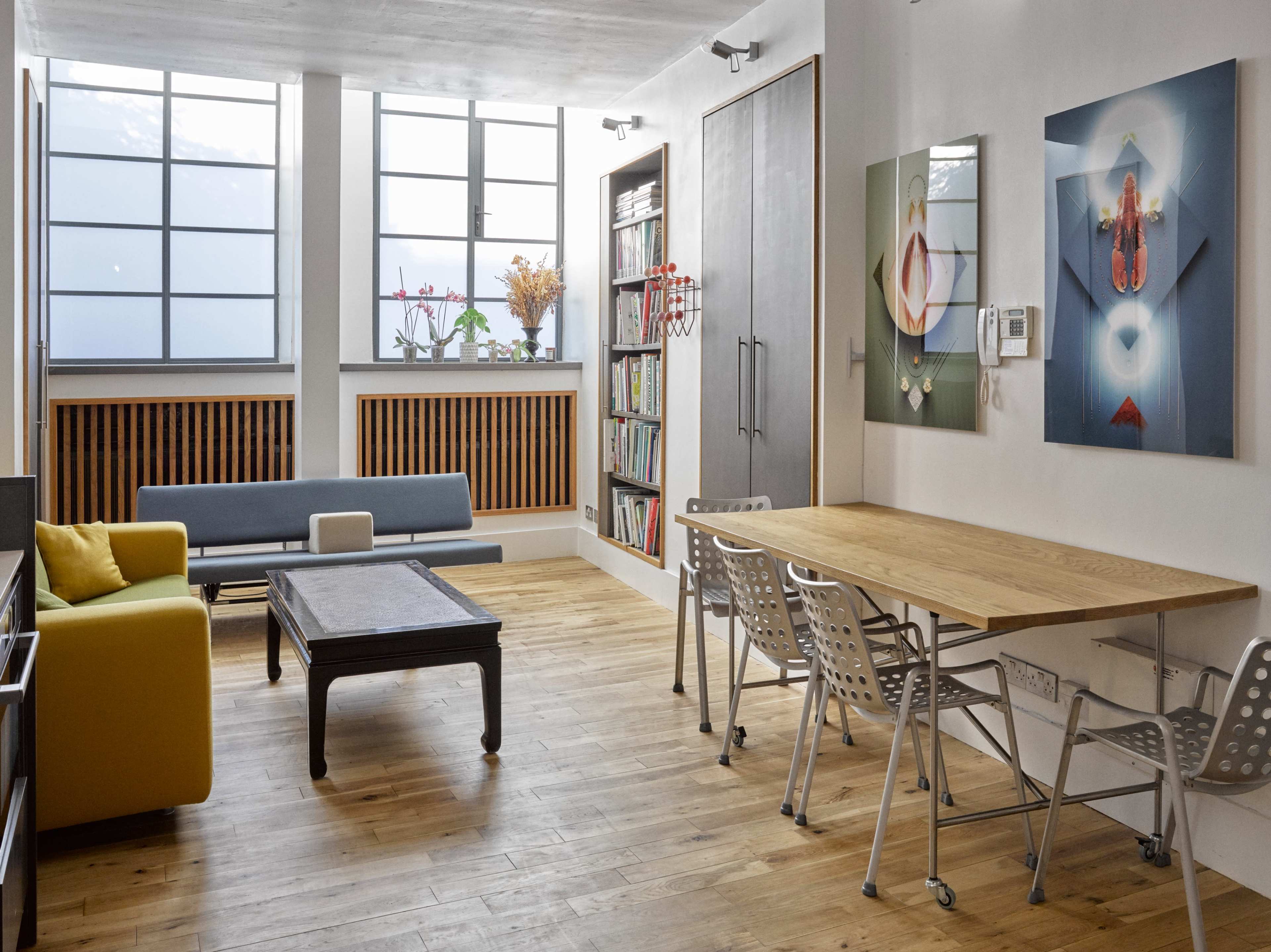The image depicts a modern, open living space featuring a blue sofa, a wooden dining table with metal chairs, and artwork on the walls.