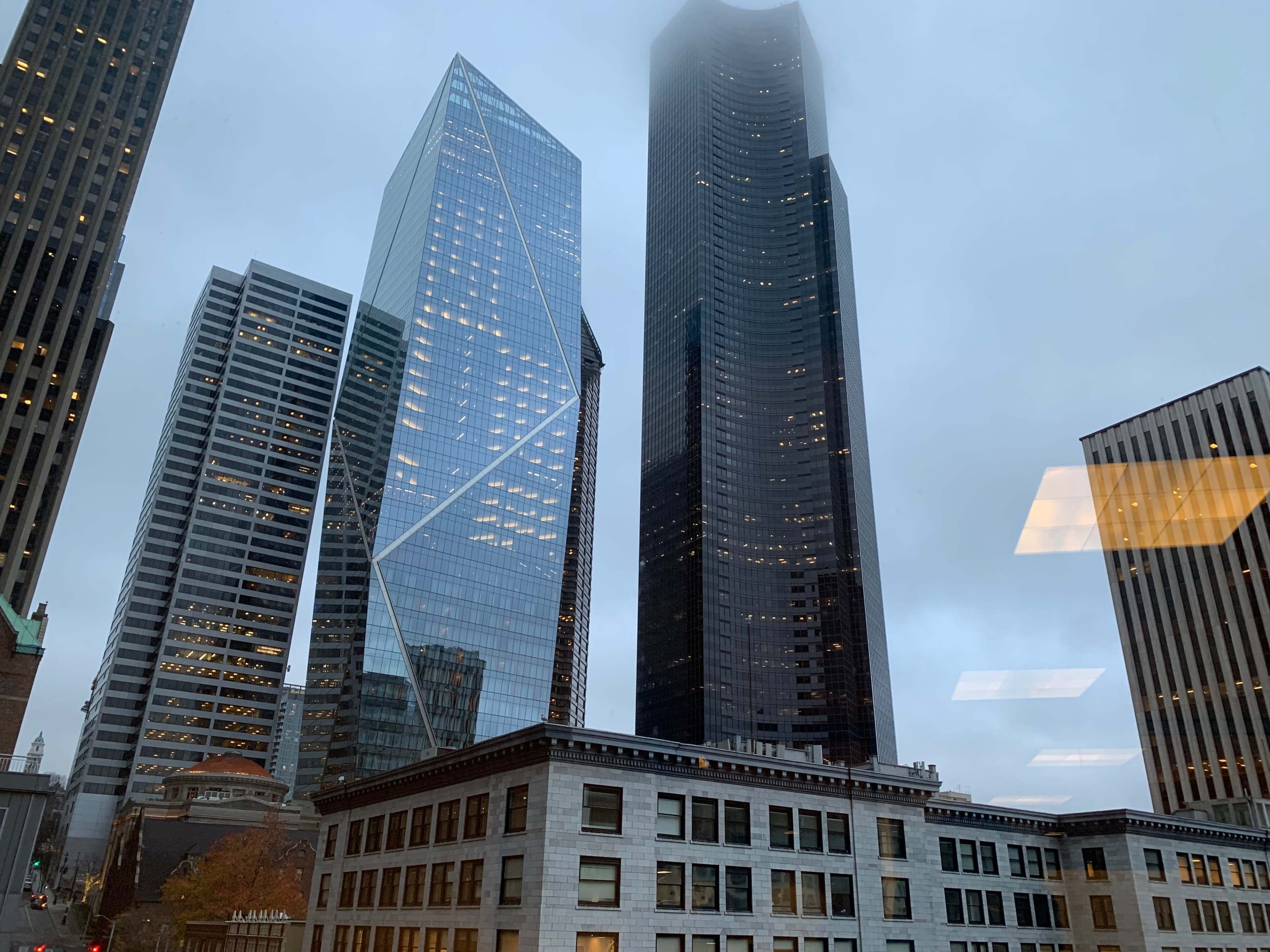 Modern skyscrapers surrounded by low clouds, with a historical building in the foreground.