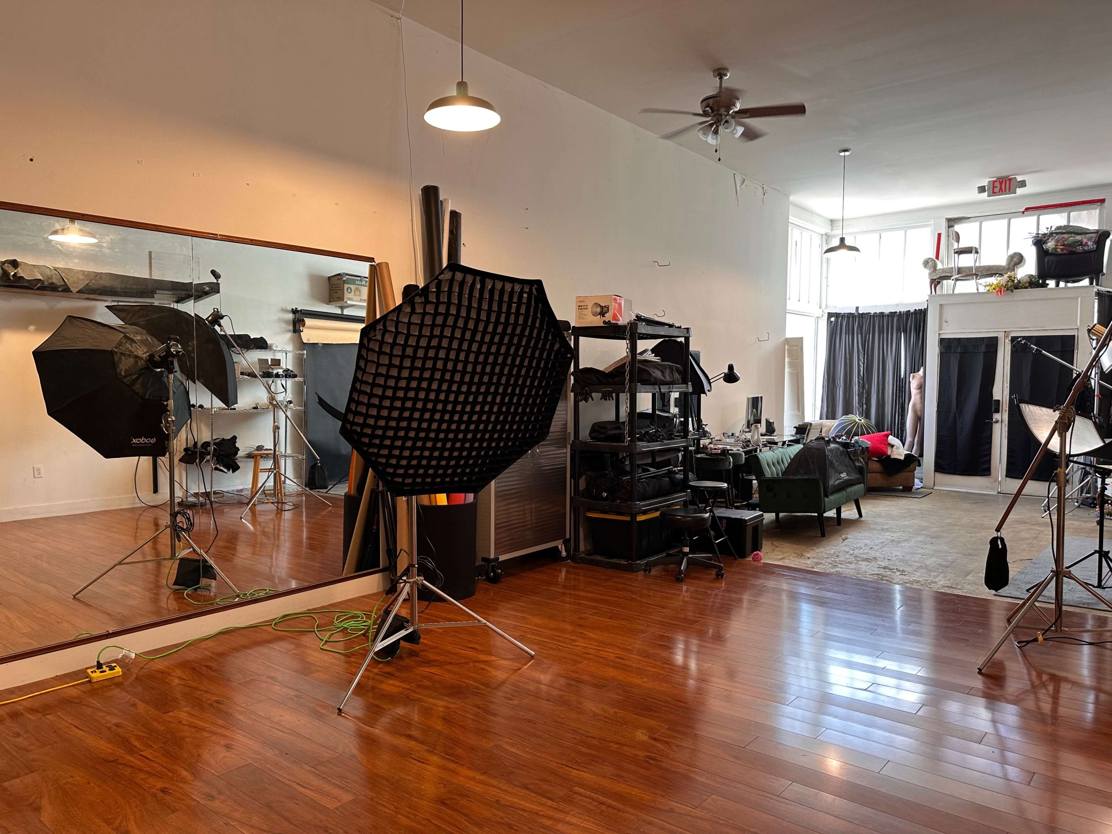 The image shows a photography studio featuring various lighting equipment, a large mirror, and a seating area in the background.