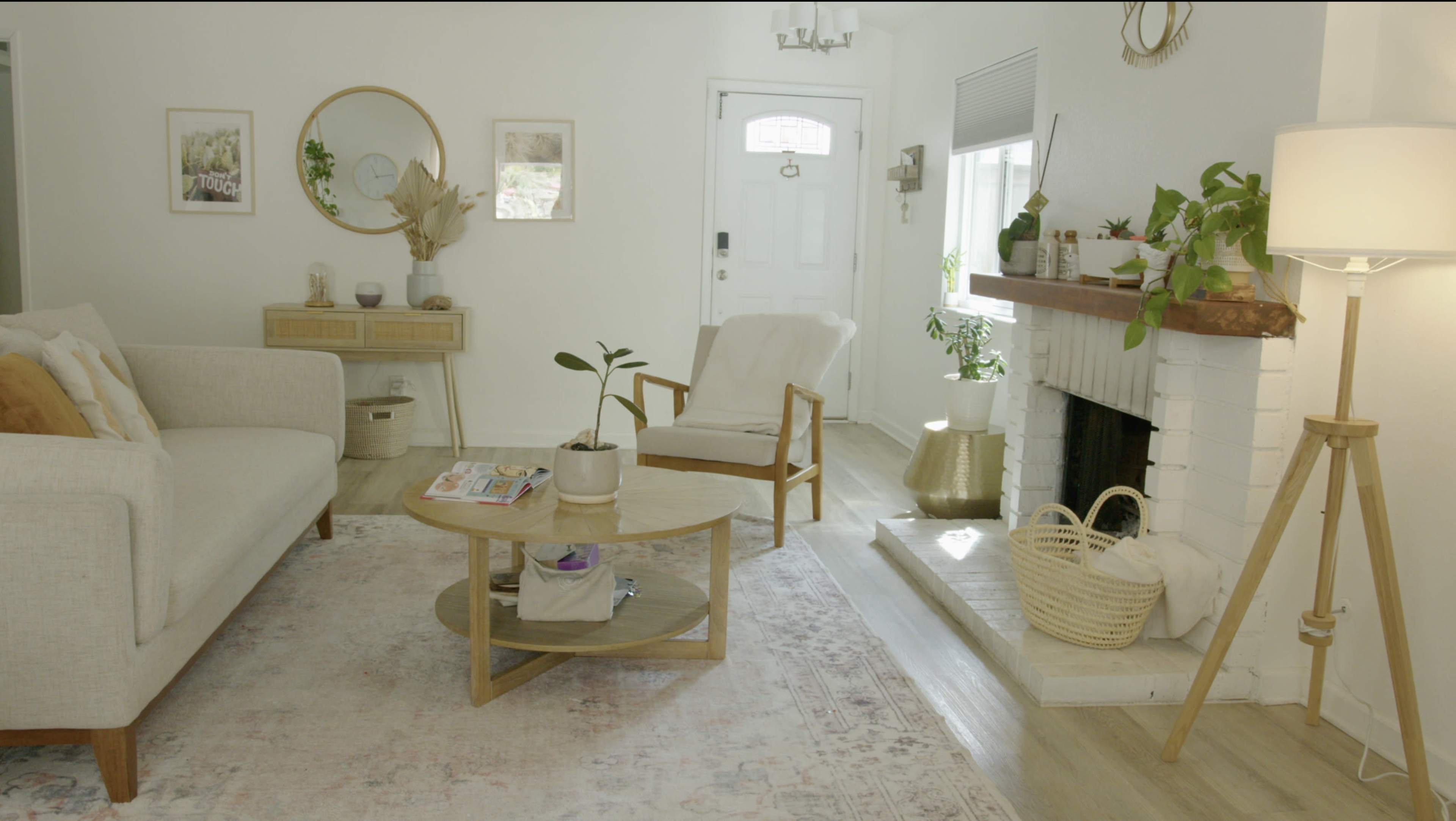 A bright living room features a cozy seating area with a round coffee table, a fireplace with plants, and a decorative mirror on the wall.