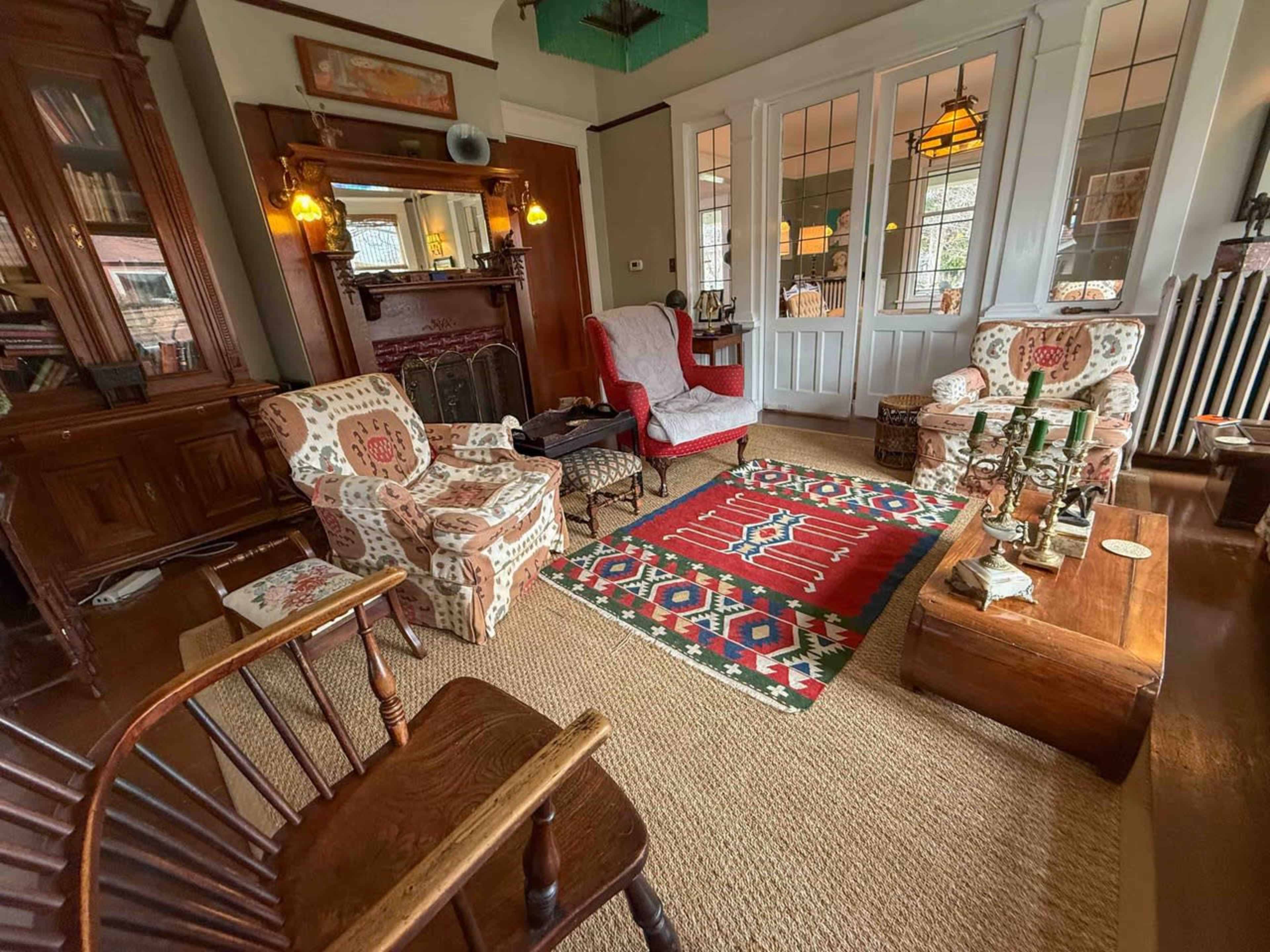 The image showcases a cozy living room with patterned armchairs, a wooden coffee table, and a decorative rug, surrounded by bookshelves and a fireplace.