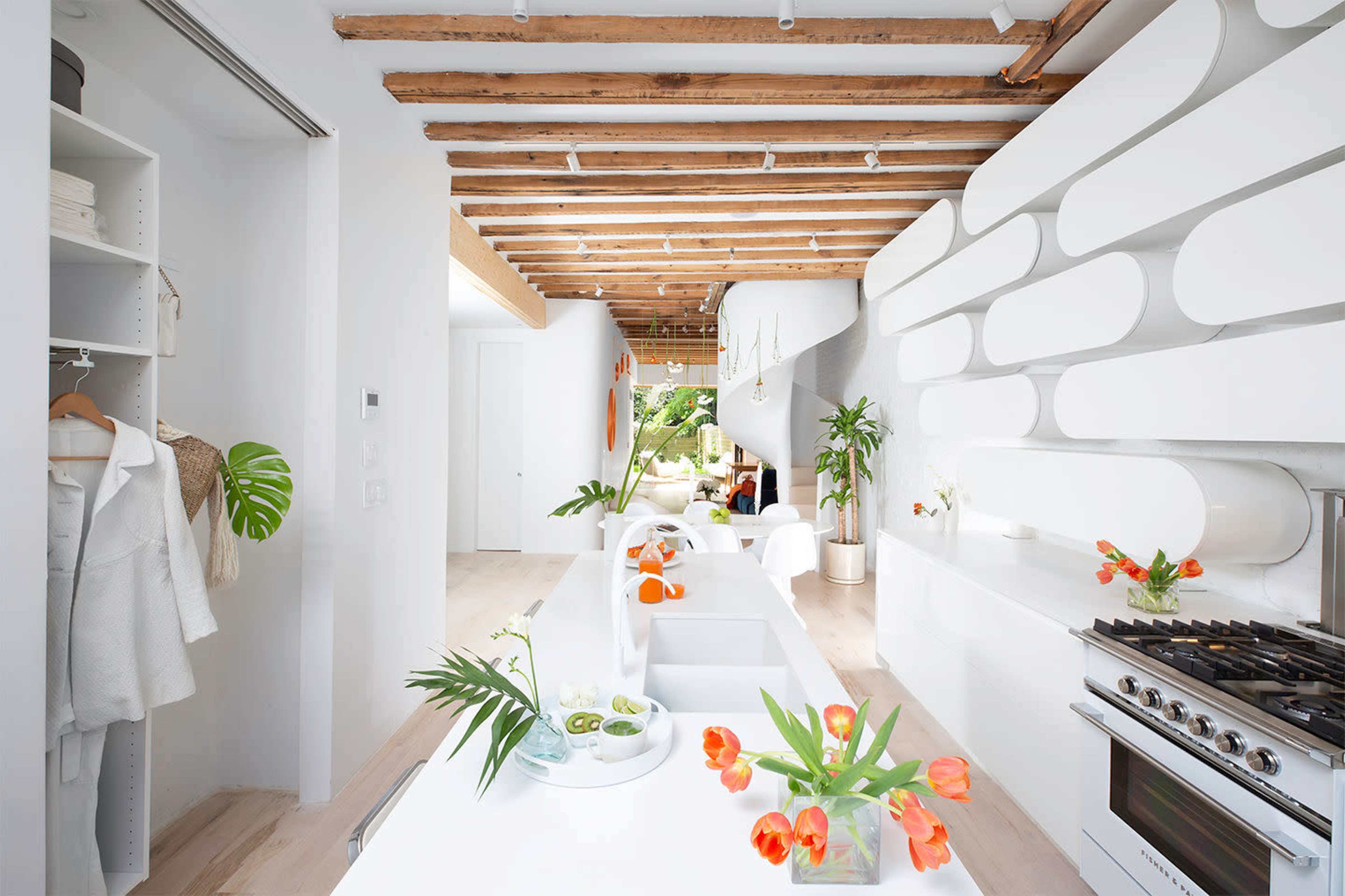 The image shows a modern kitchen with exposed wooden beams, a long white countertop, and decorative plants.