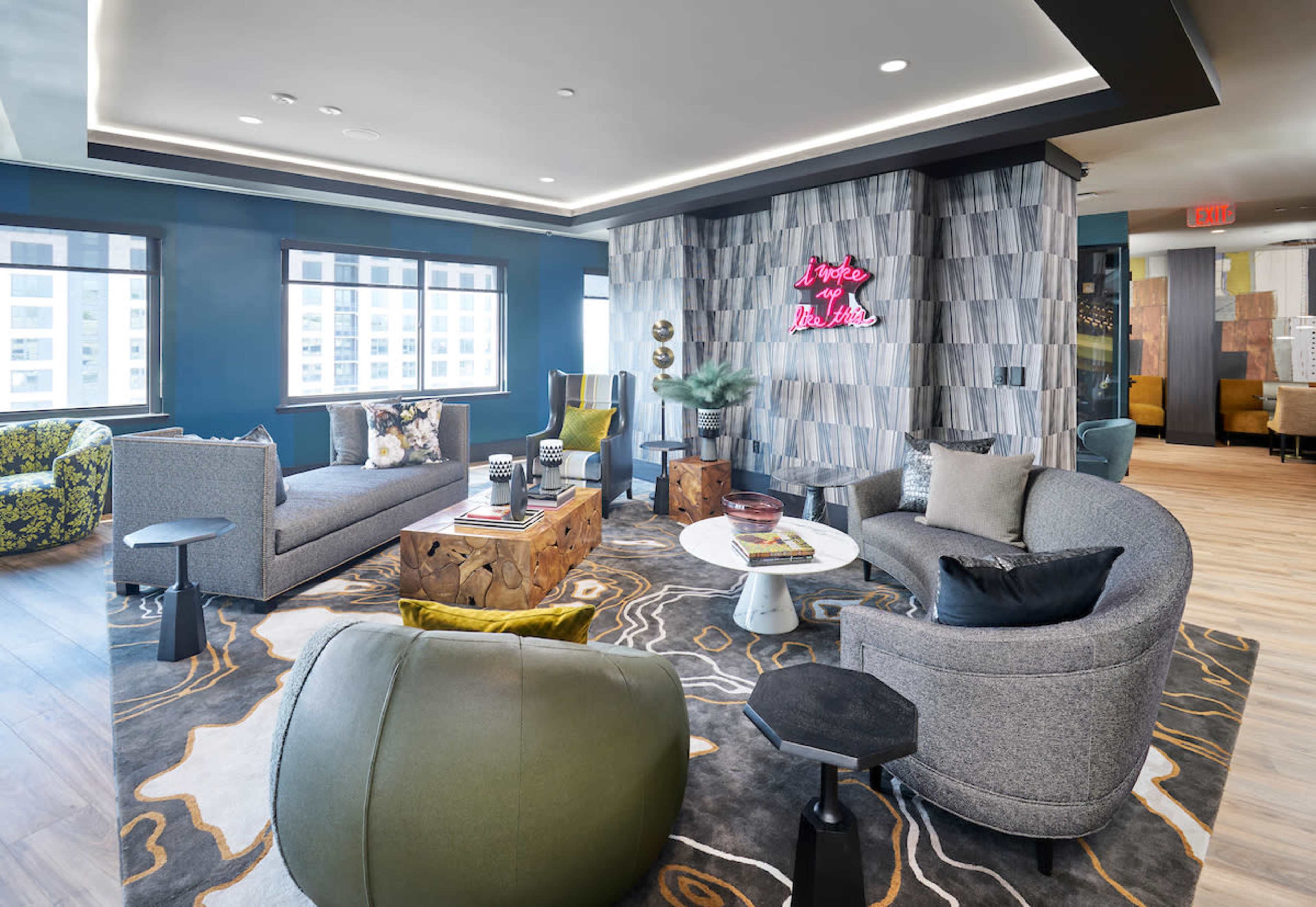 A modern lounge area with various seating arrangements, including couches and chairs, centered around decorative coffee tables and illuminated by neon signage.