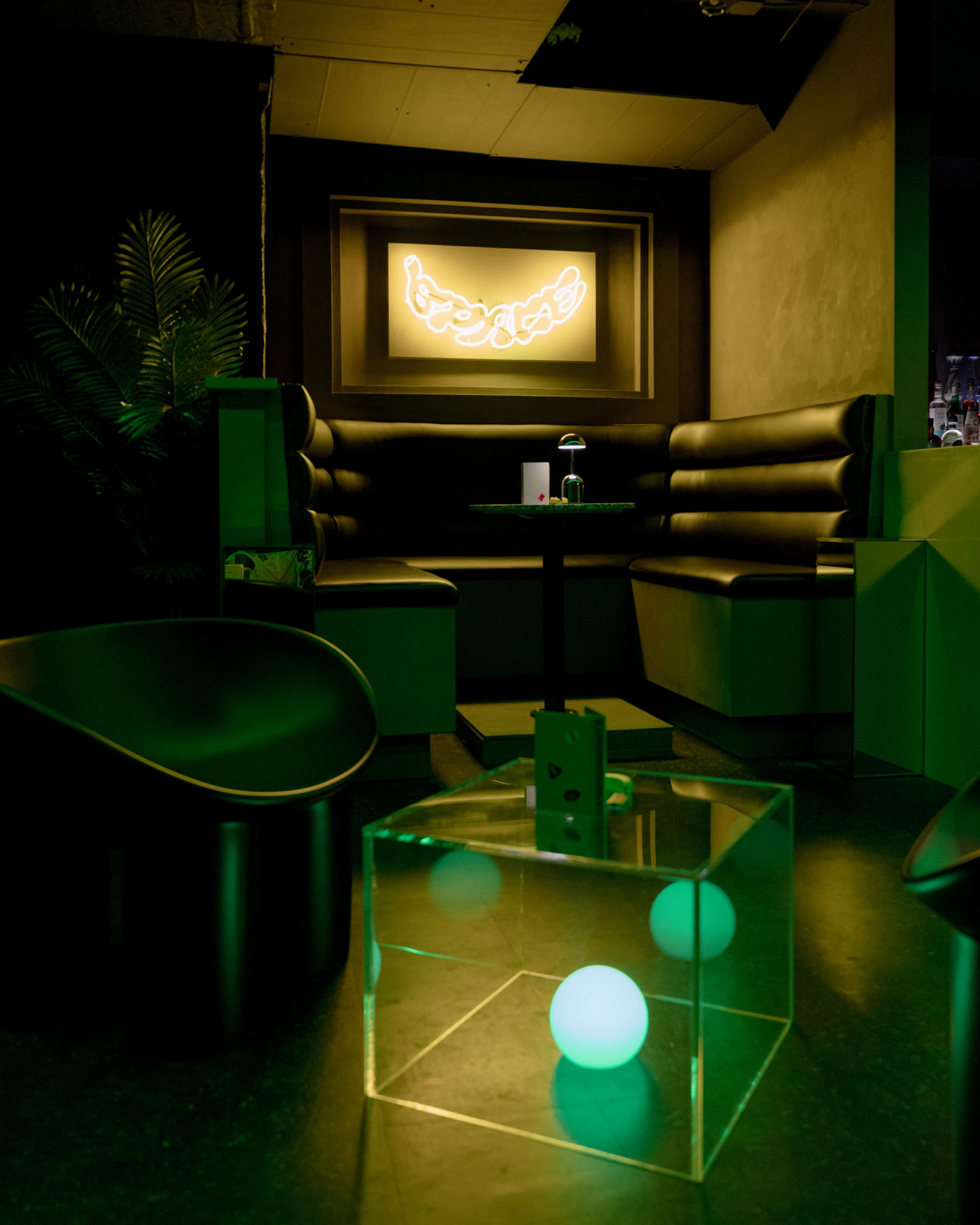 A modern lounge area features black leather seating, a glowing neon sign on the wall, and a transparent cube containing glowing orbs.