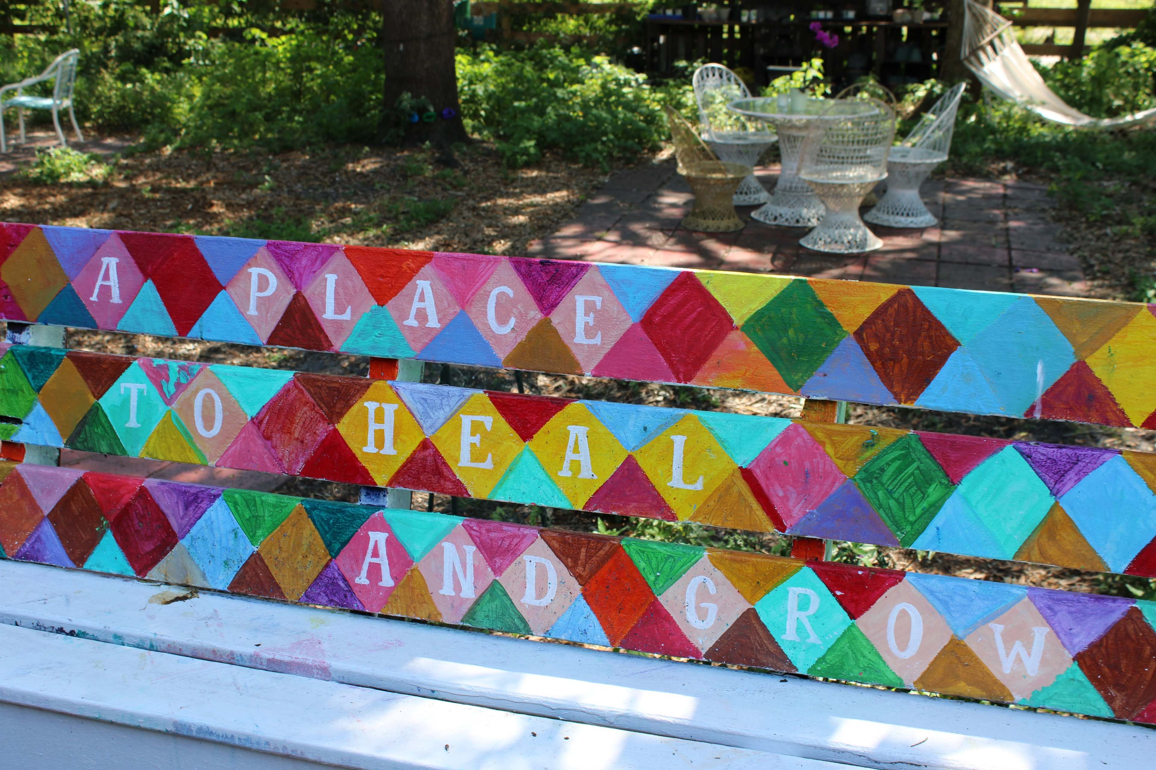 A wooden bench features colorful triangular patterns with the words "A PLACE TO HEAL AND GROW" painted on it.