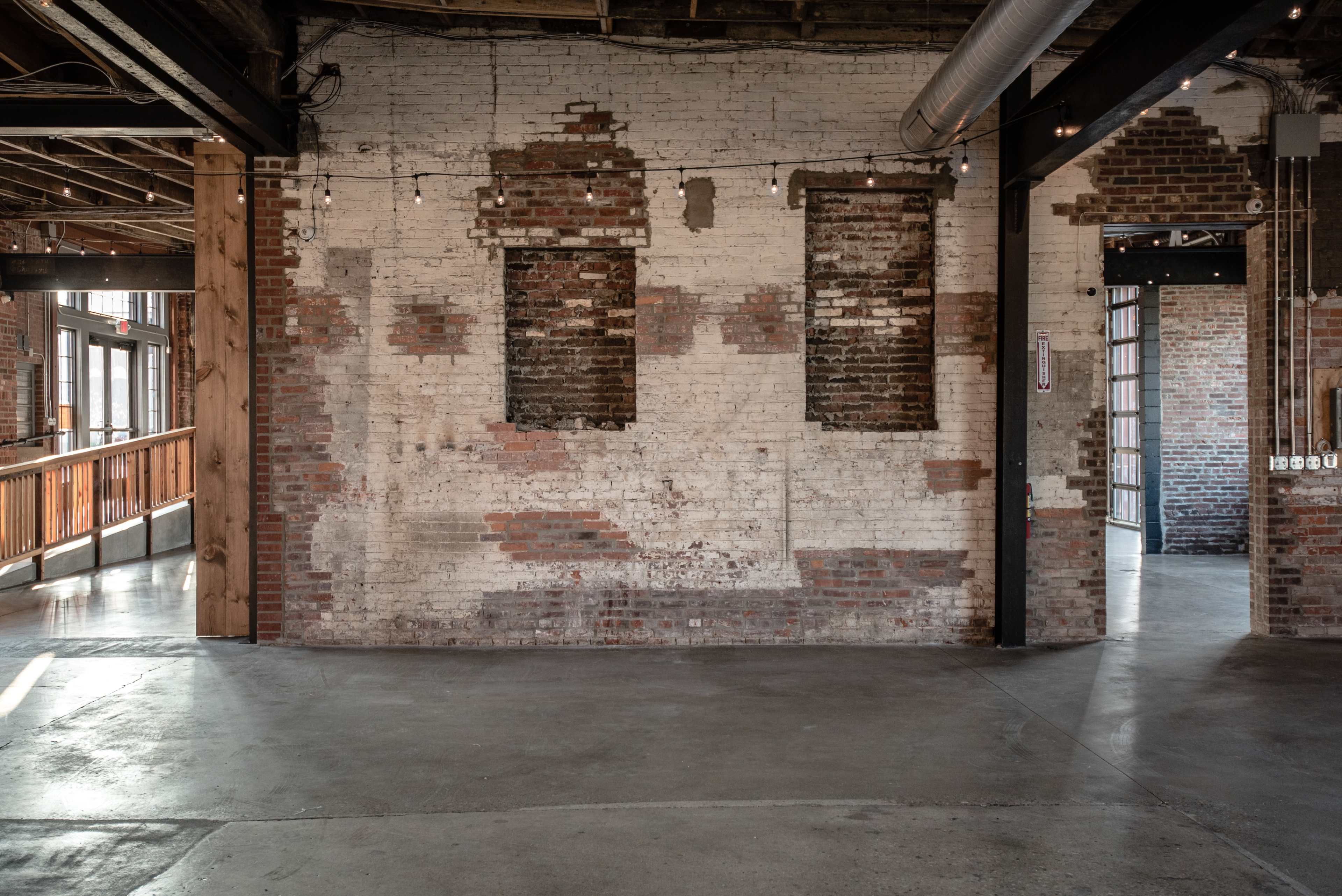 An industrial-style interior with exposed brick walls and concrete flooring, featuring two empty window frames.