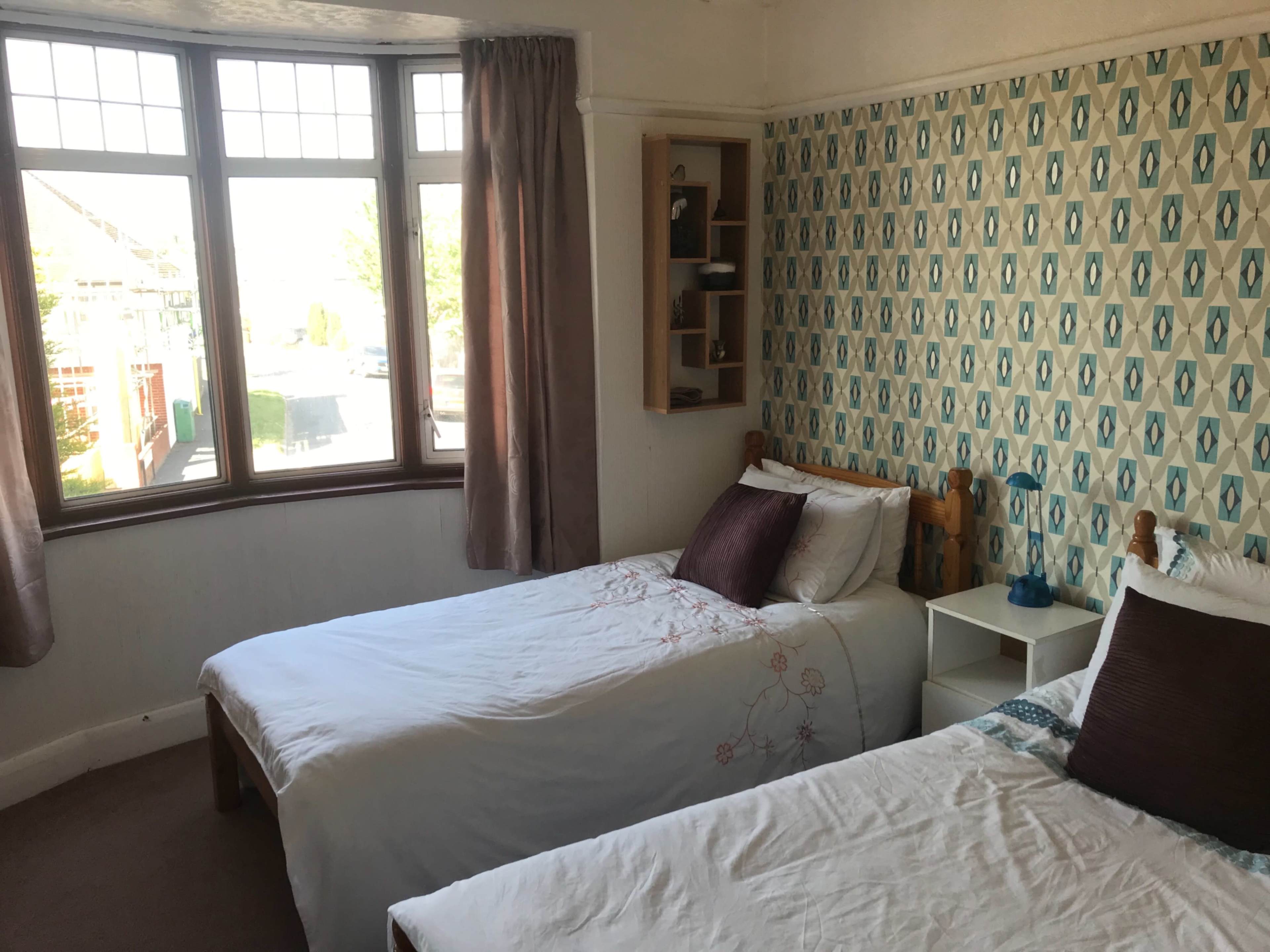A bedroom with two single beds, a window with curtains, and patterned wallpaper.