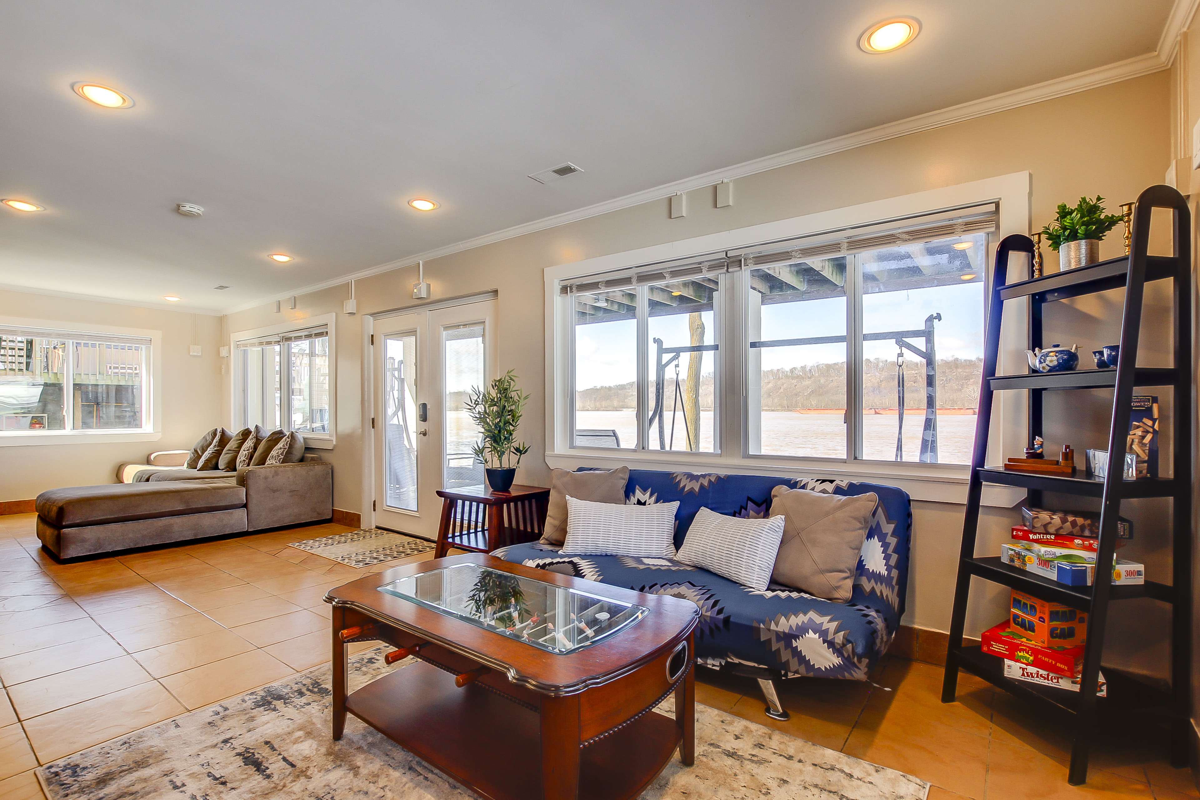 A bright living area features a blue patterned sofa, a coffee table, and large windows overlooking a body of water.