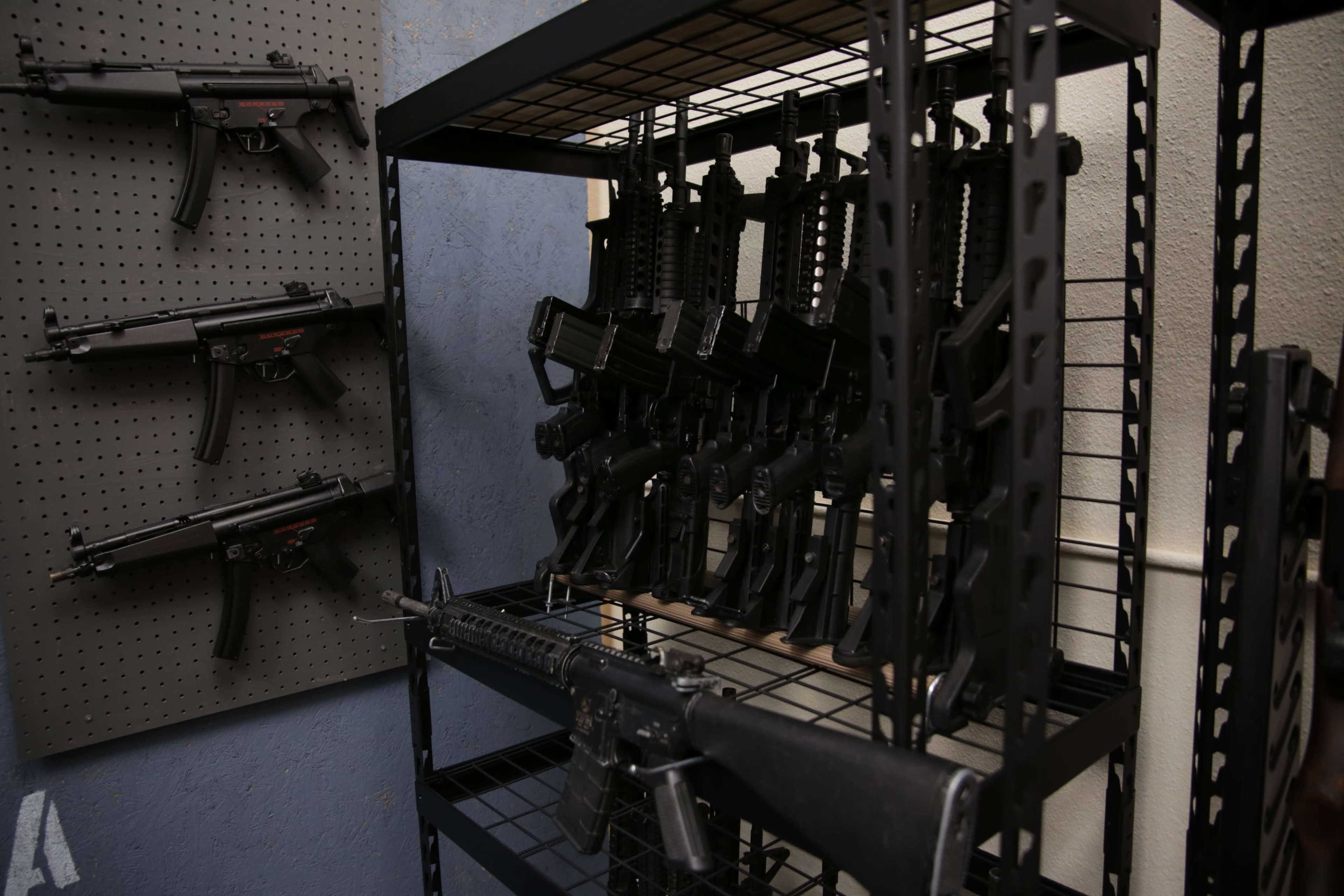 A metal shelving unit displays various firearms, with several rifles and handguns arranged neatly.