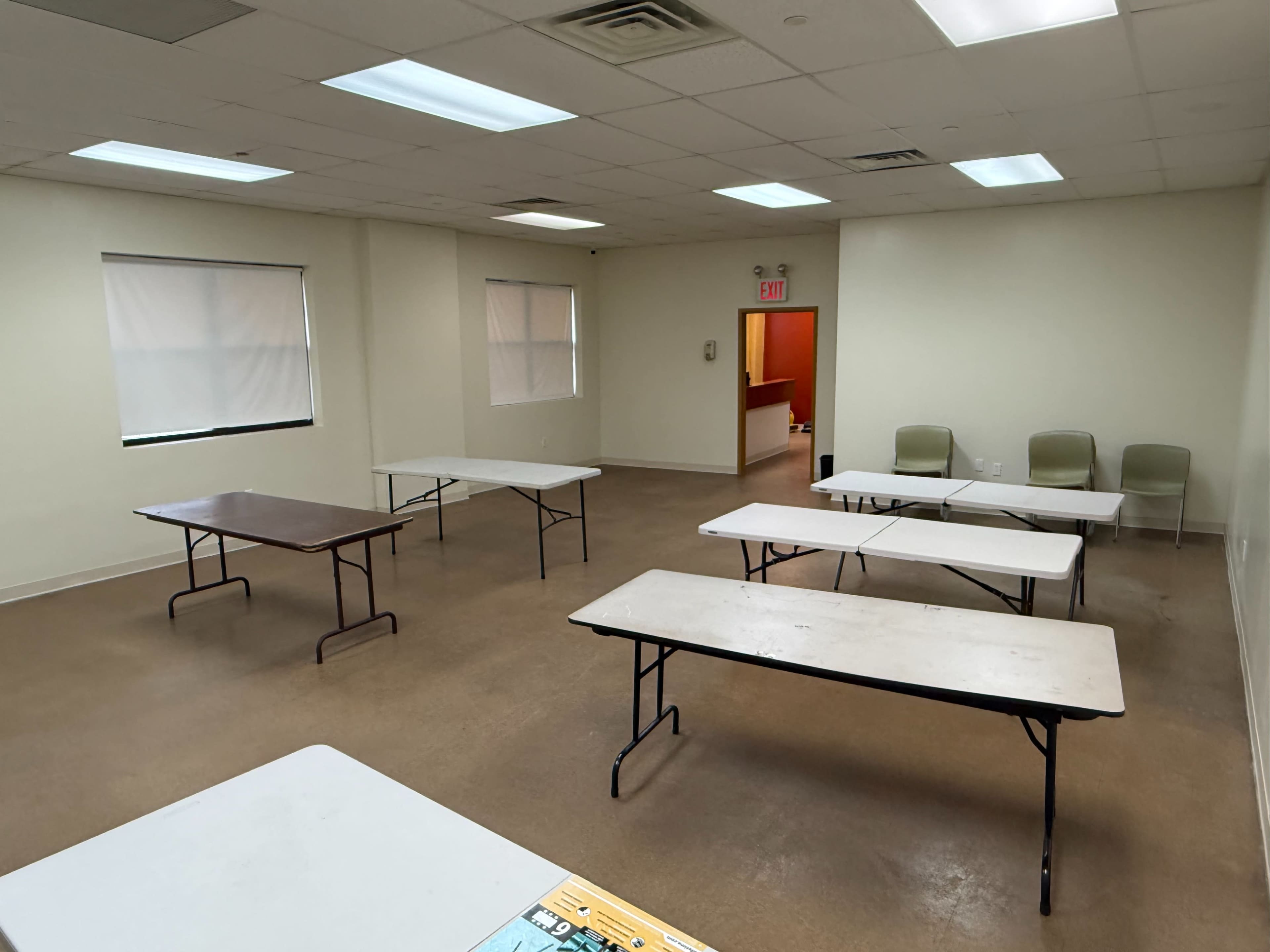 The image shows a spacious room with several folding tables arranged in various positions and a few chairs along one wall.