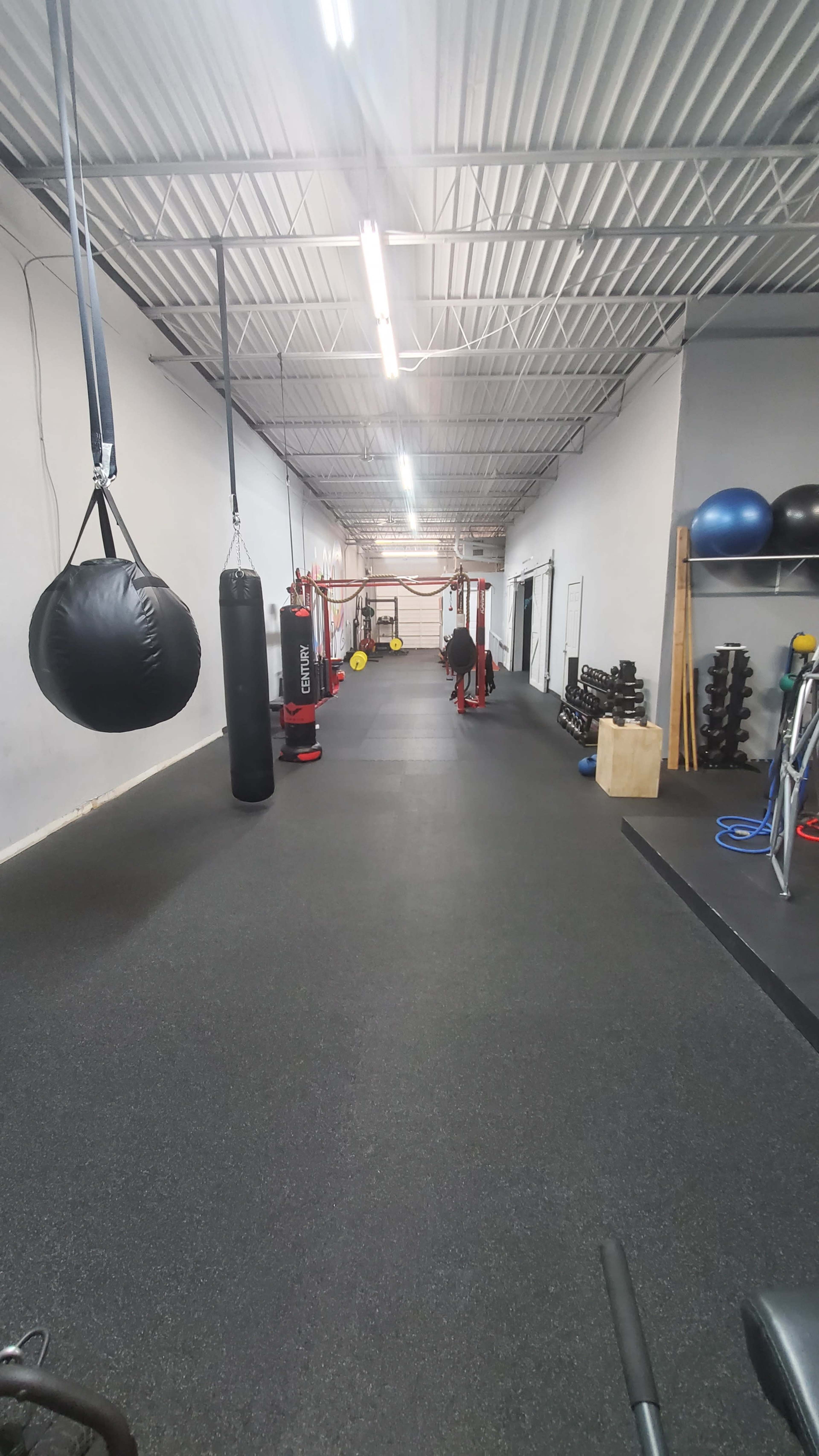 A spacious gym interior with various exercise equipment, including punching bags, weights, and fitness balls lined against the walls.