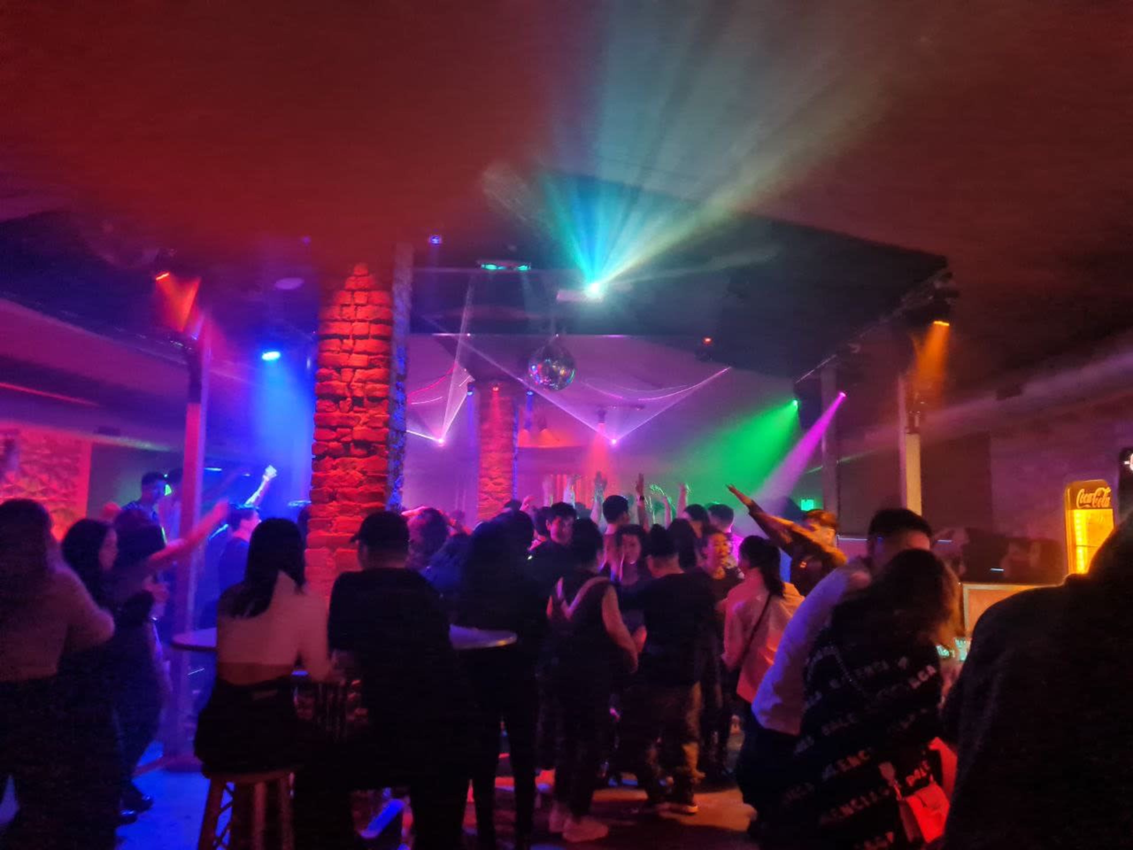 A dimly lit nightclub filled with people dancing under colorful lights and a disco ball.