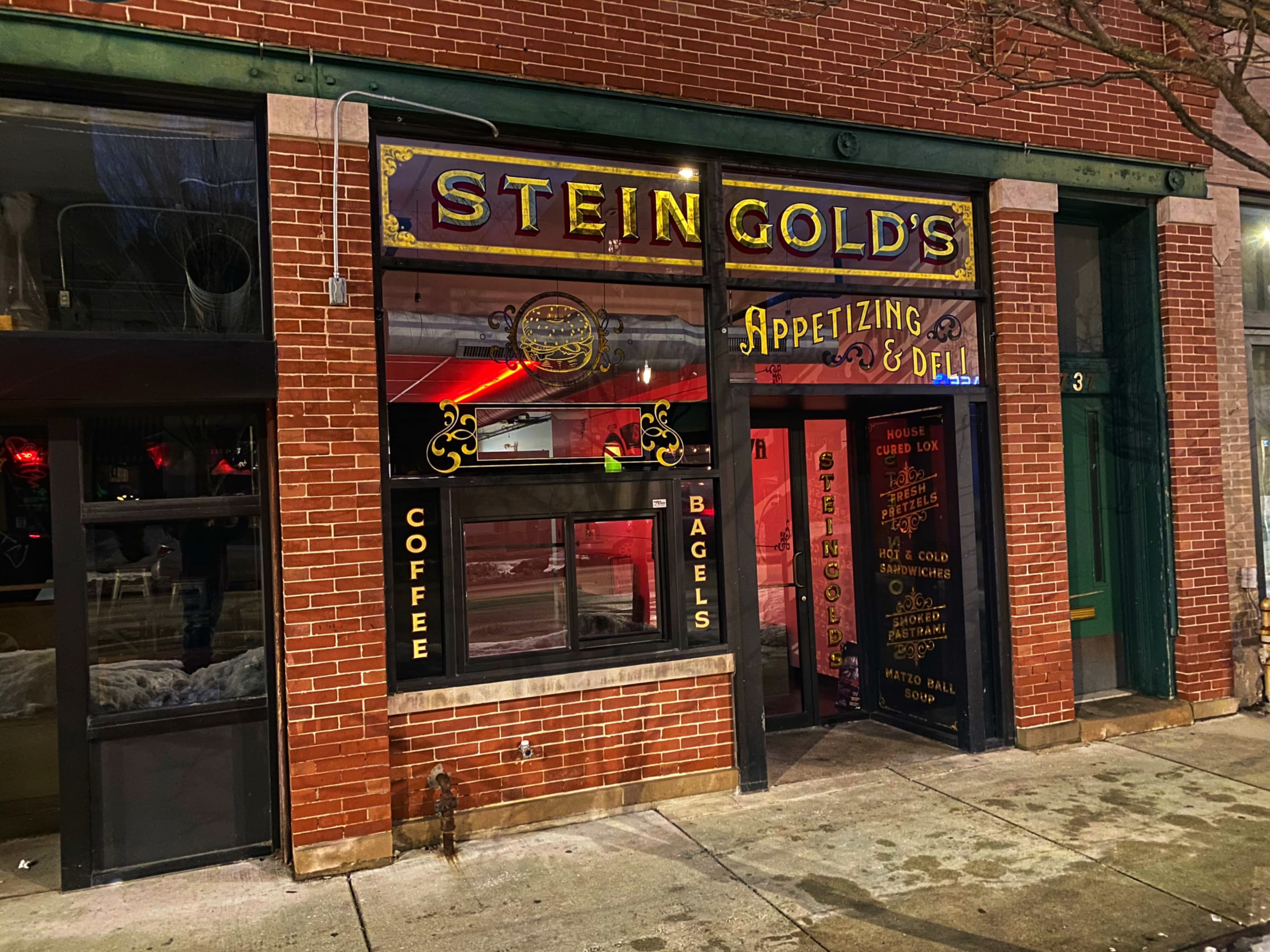 The image shows a brick storefront with a sign reading "Steingold's Appetizing & Deli," featuring window displays for coffee and bagels.