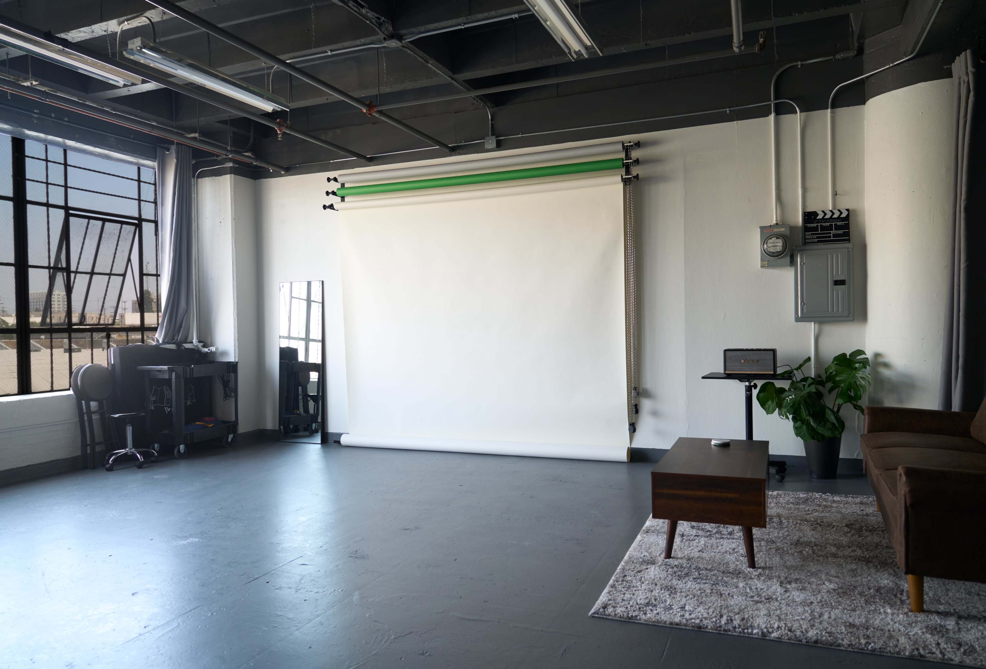 A photography studio features a blank backdrop, a brown sofa, a small table, and a workspace with a mirror and electronic equipment.