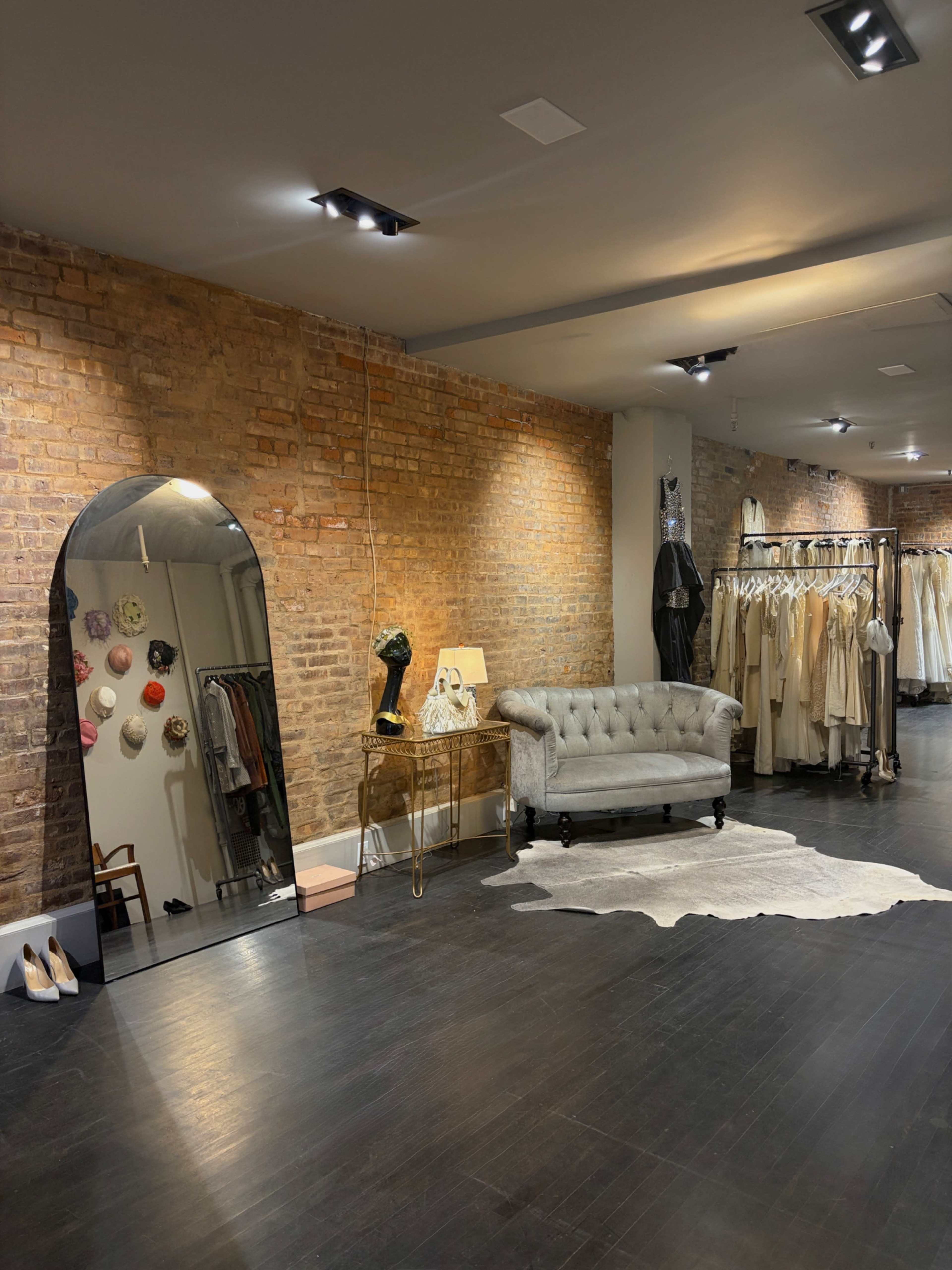 The image shows a stylish boutique with exposed brick walls, a tufted gray sofa, and a rack of hanging clothing.