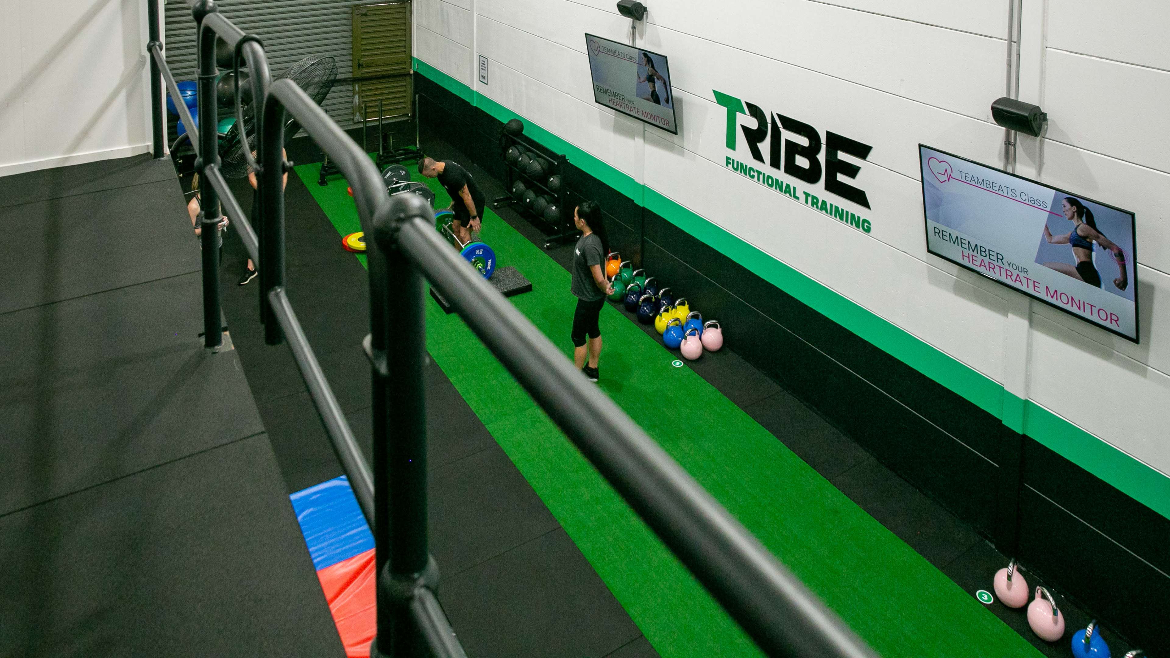 A gym space with a workout area featuring weights, kettlebells, and exercise equipment, along with monitors displaying training information on the walls.