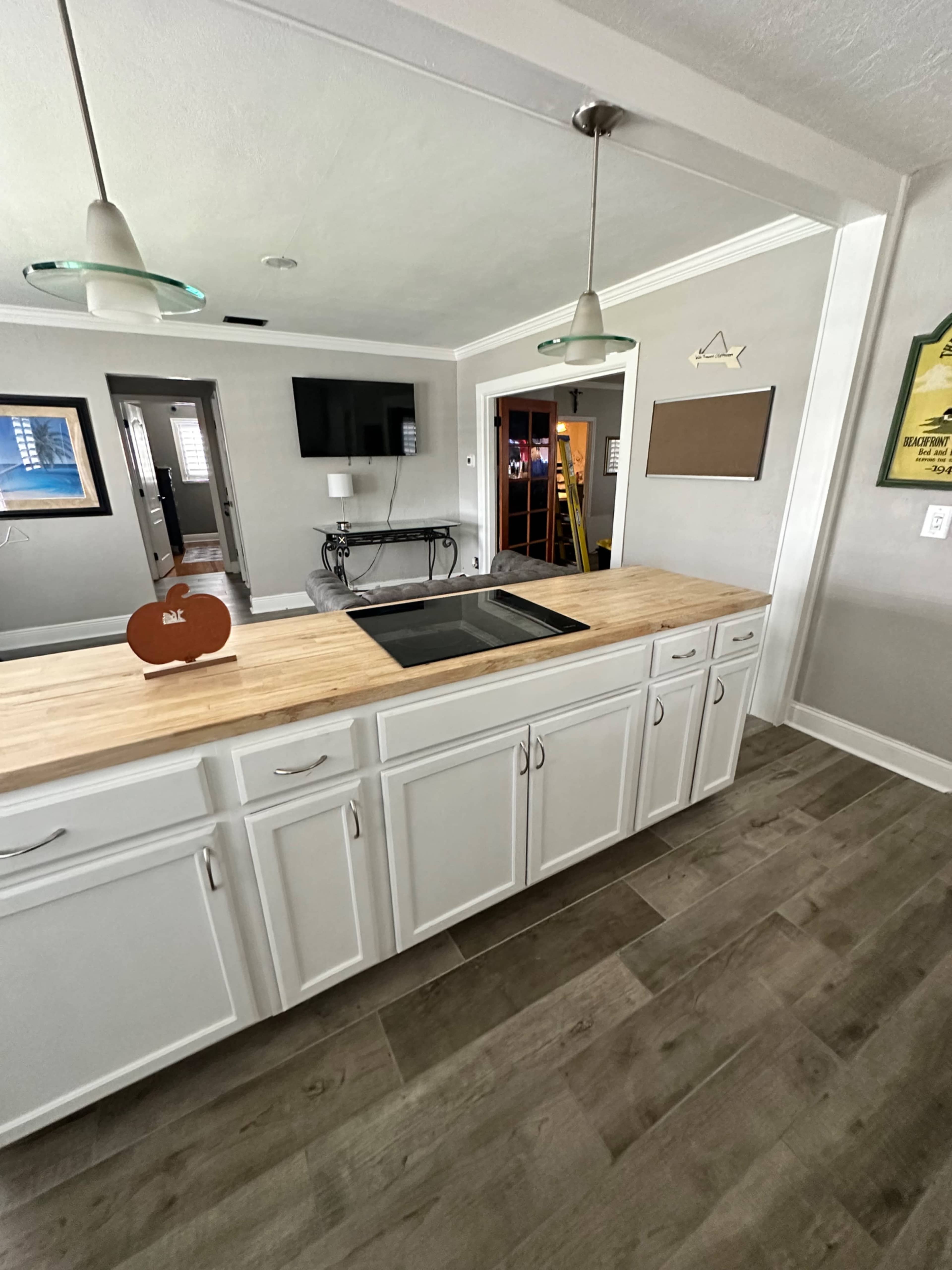 A modern kitchen with a wooden countertop island, white cabinetry, and pendant lights above.