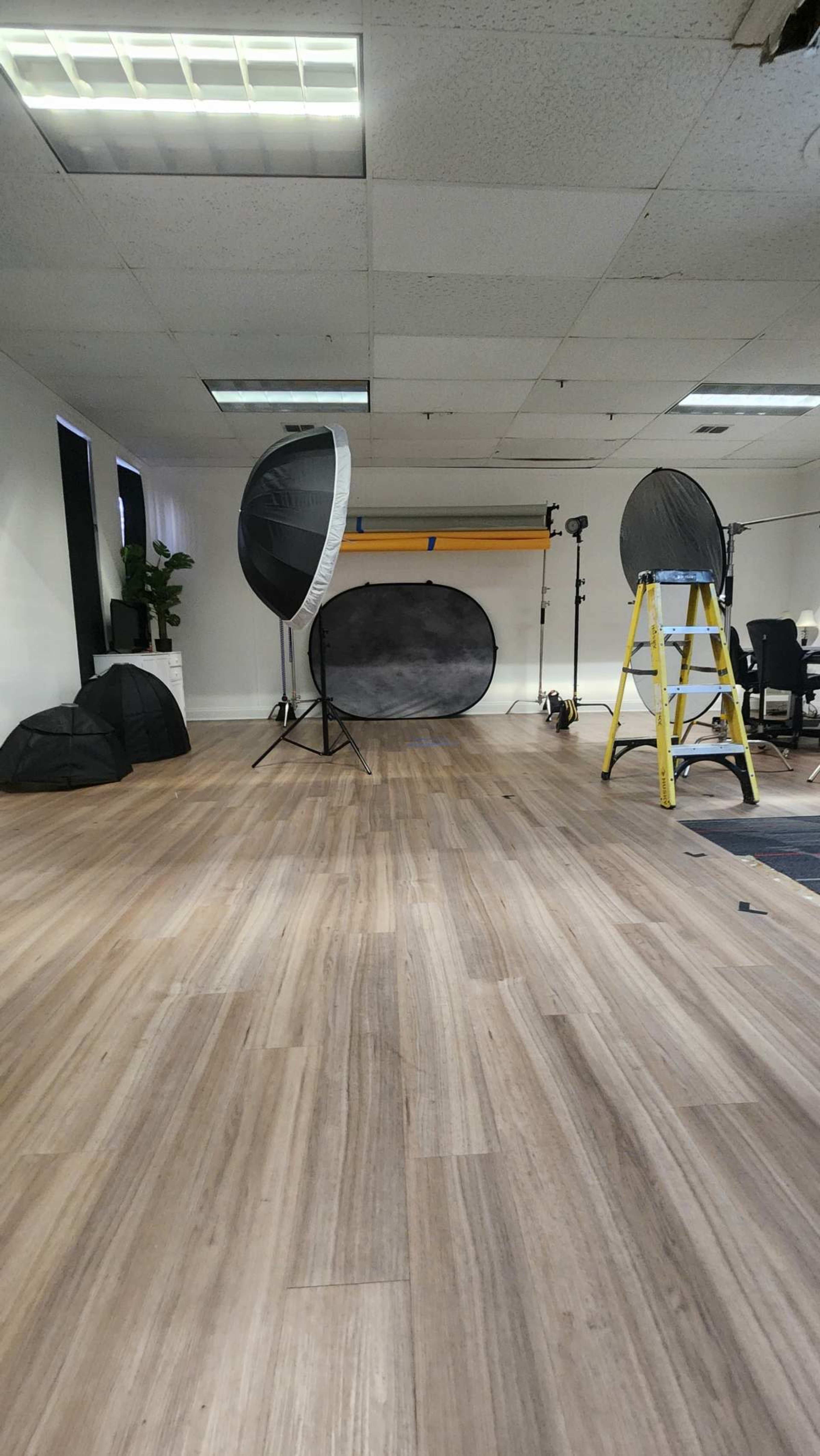 The image shows a spacious photography studio with various lighting equipment, backdrops, and a ladder set up on the floor.