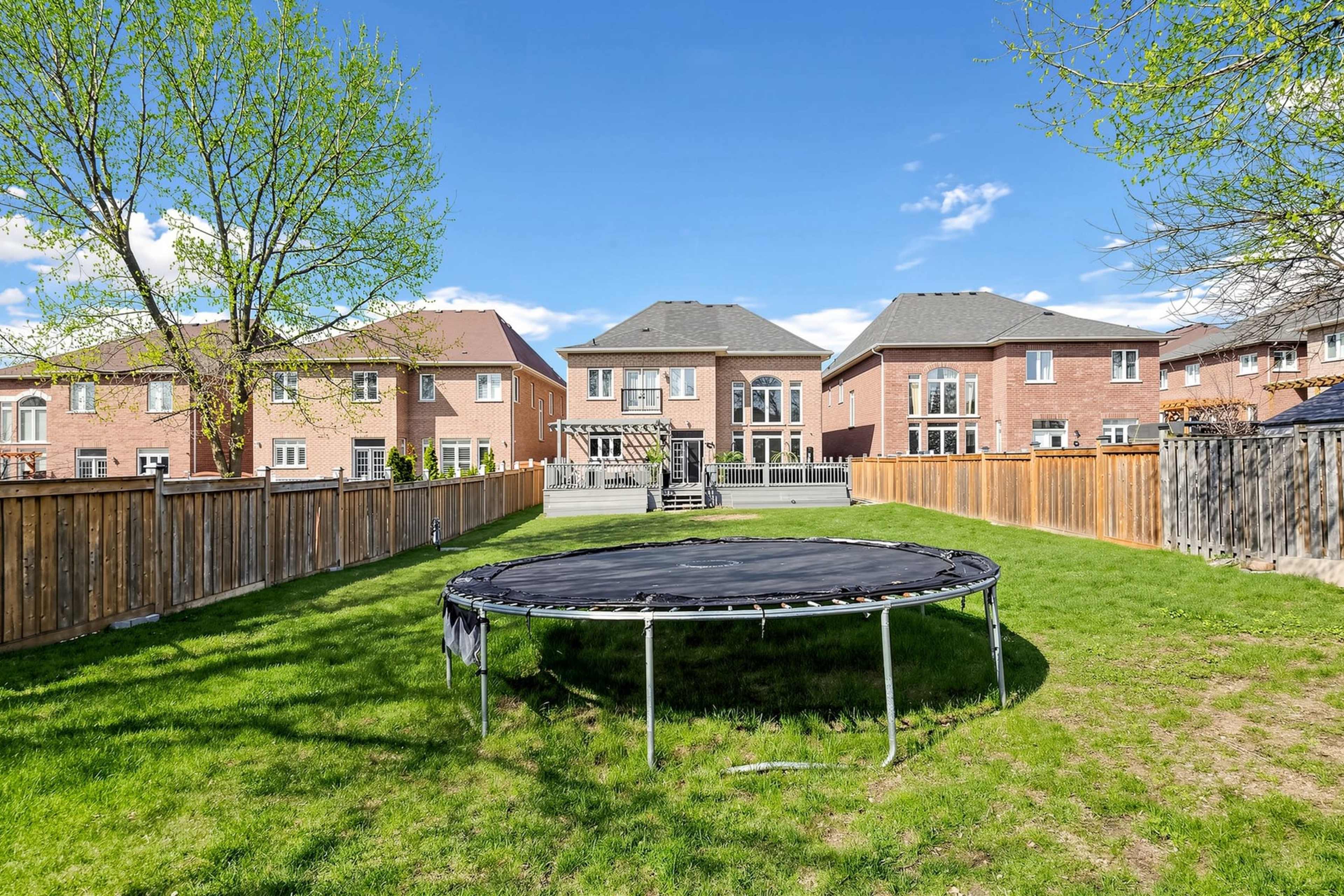 The image shows a backyard with a trampoline, grass, and several houses in the background.