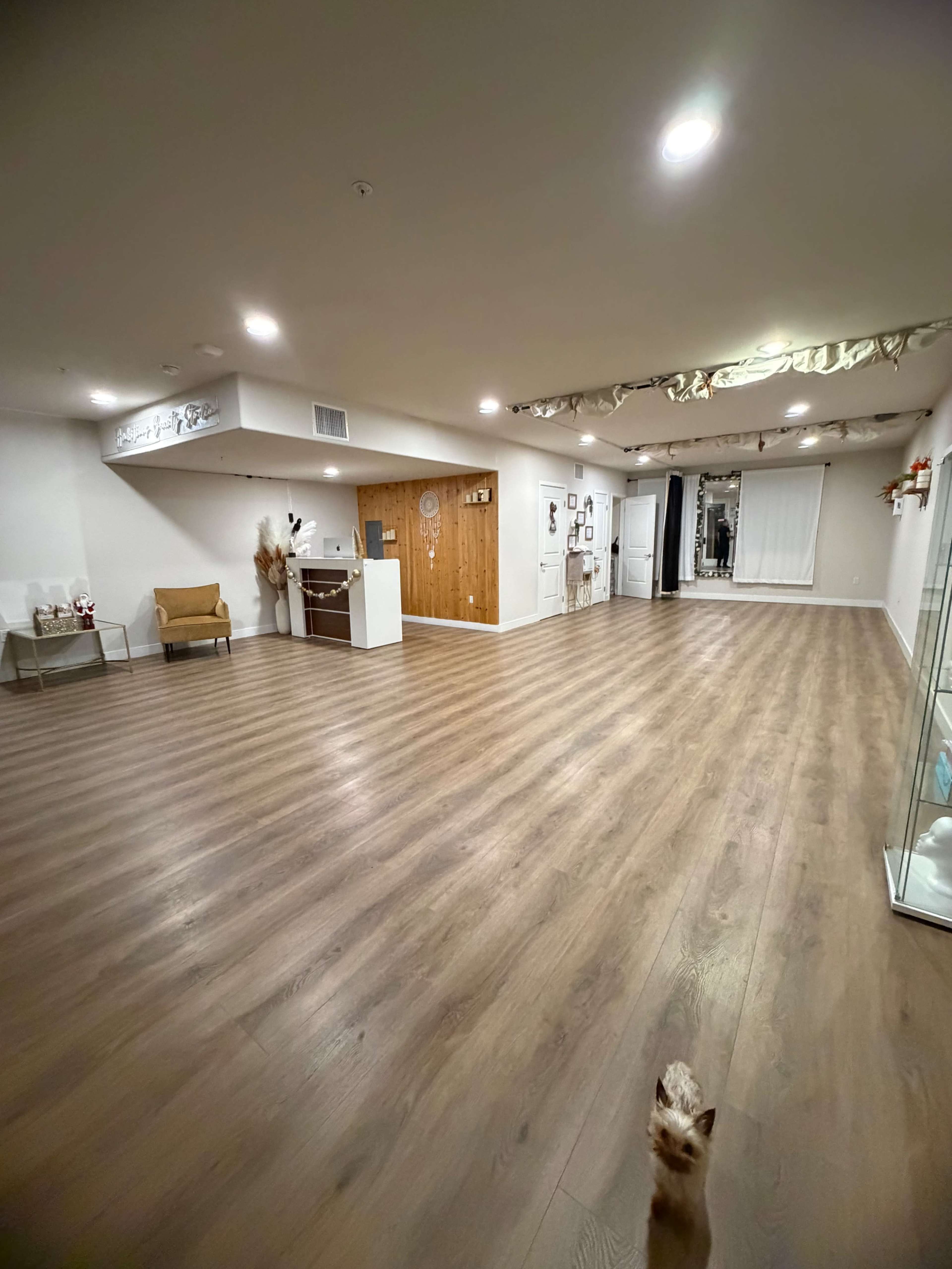 The image shows a spacious, well-lit interior room with wooden flooring and various decorative elements along the walls.