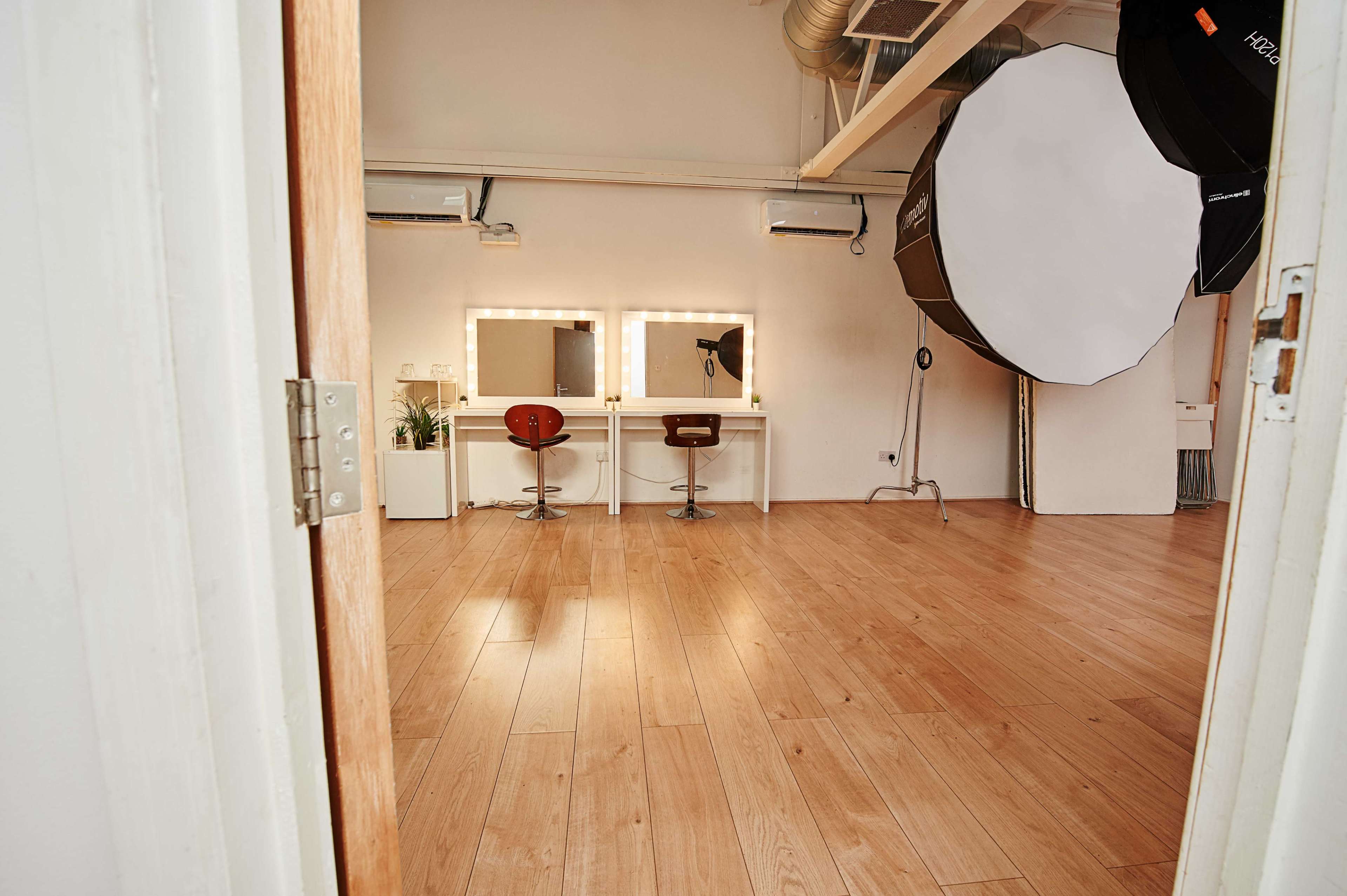 A spacious room with two vanity stations featuring mirrors and chairs, along with a large softbox lighting setup in the corner.