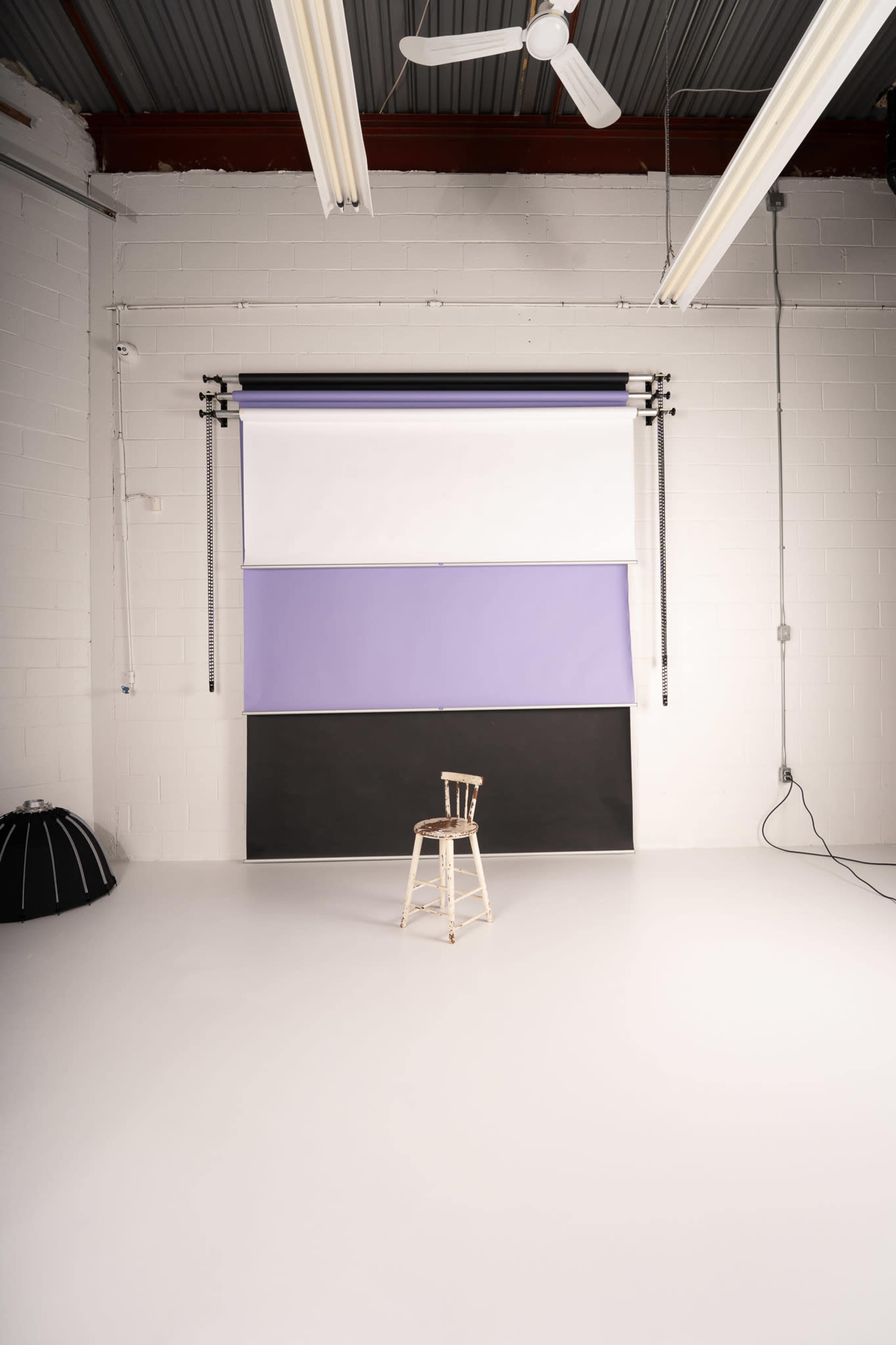 A single wooden chair is positioned in front of a backdrop consisting of multiple colored panels in a spacious, well-lit photography studio.