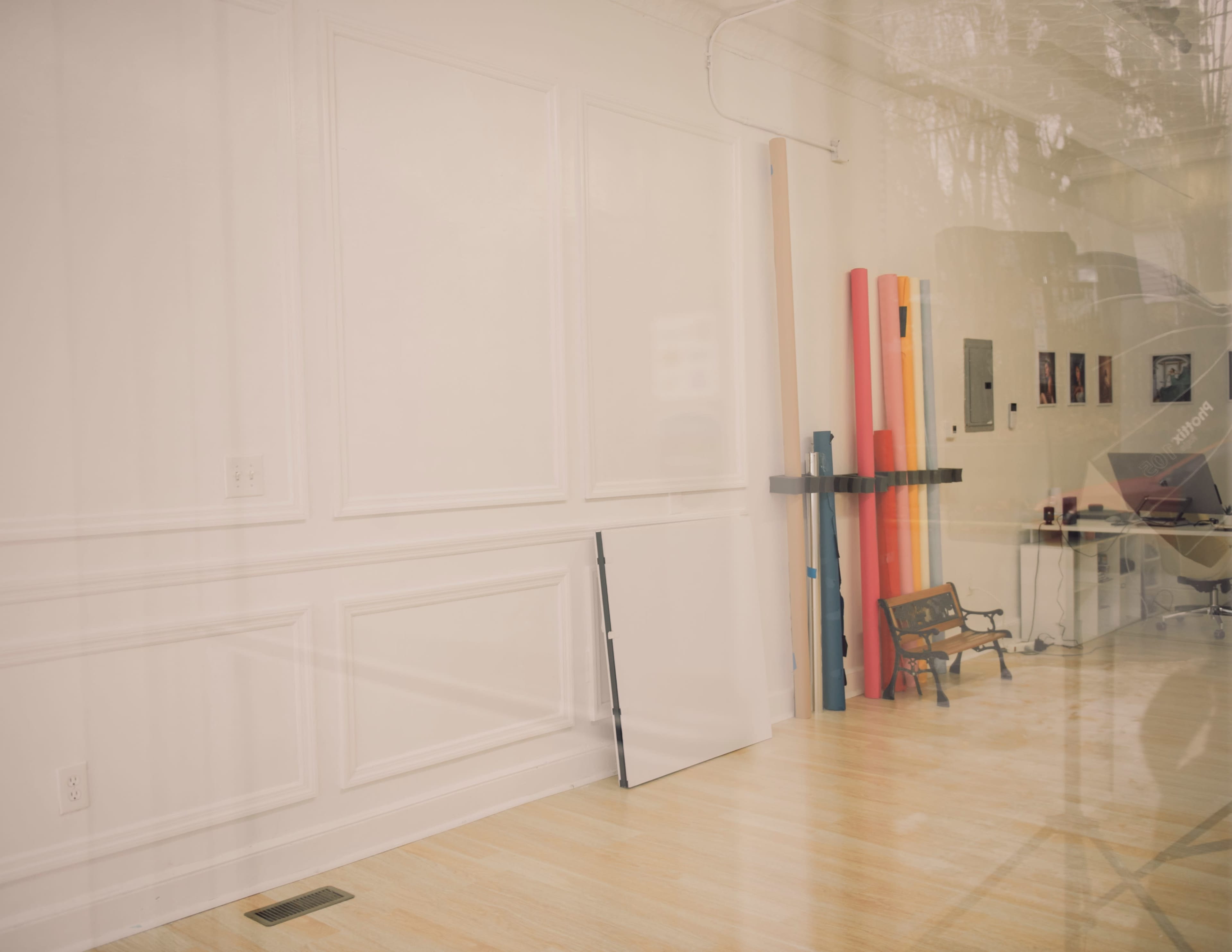 An empty room with wooden flooring, a blank wall, and a collection of brightly colored rolls leaning against the wall.