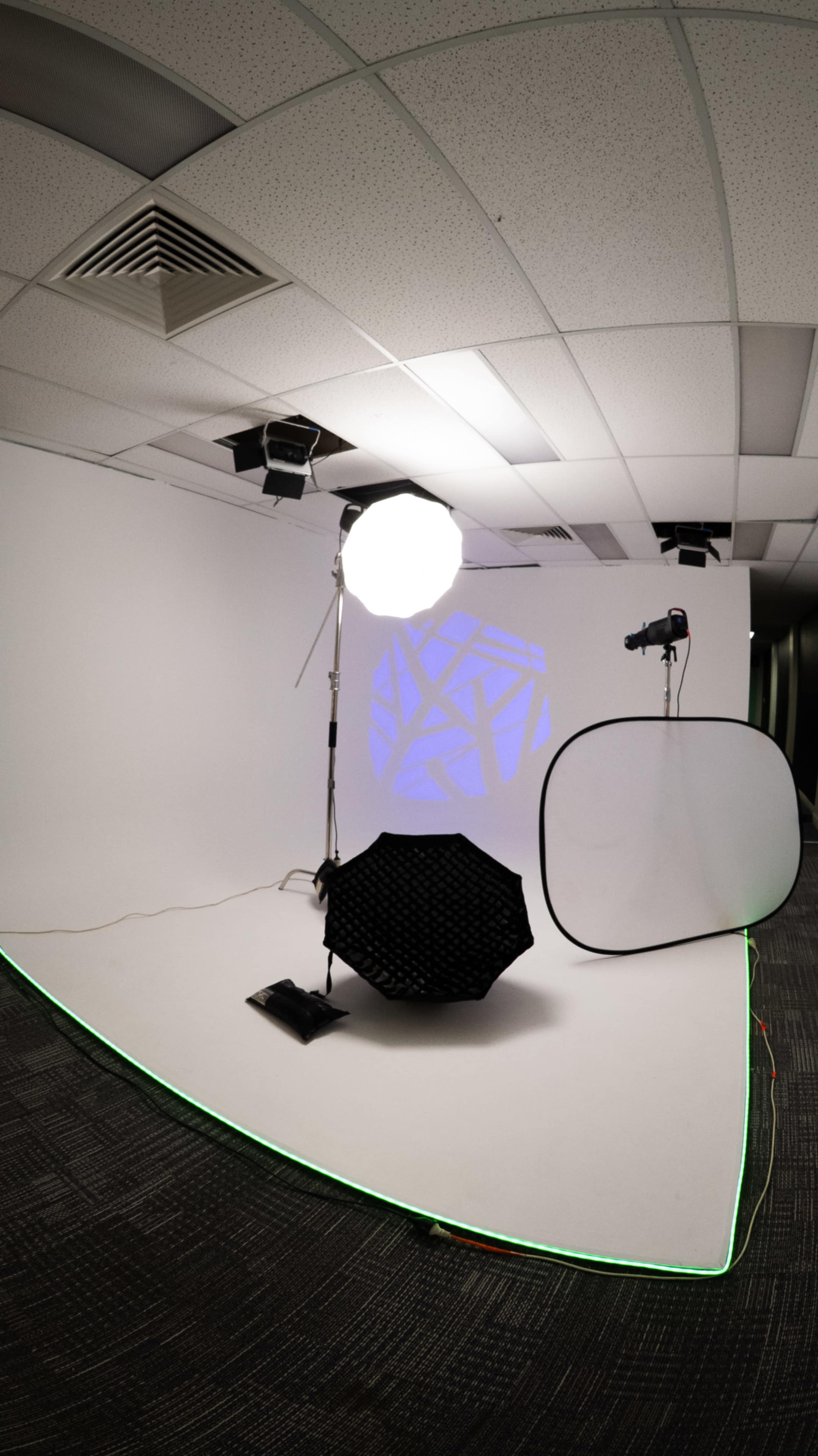 A photography studio setup features a white backdrop with a softbox, an umbrella reflector, and a light positioned on stands.