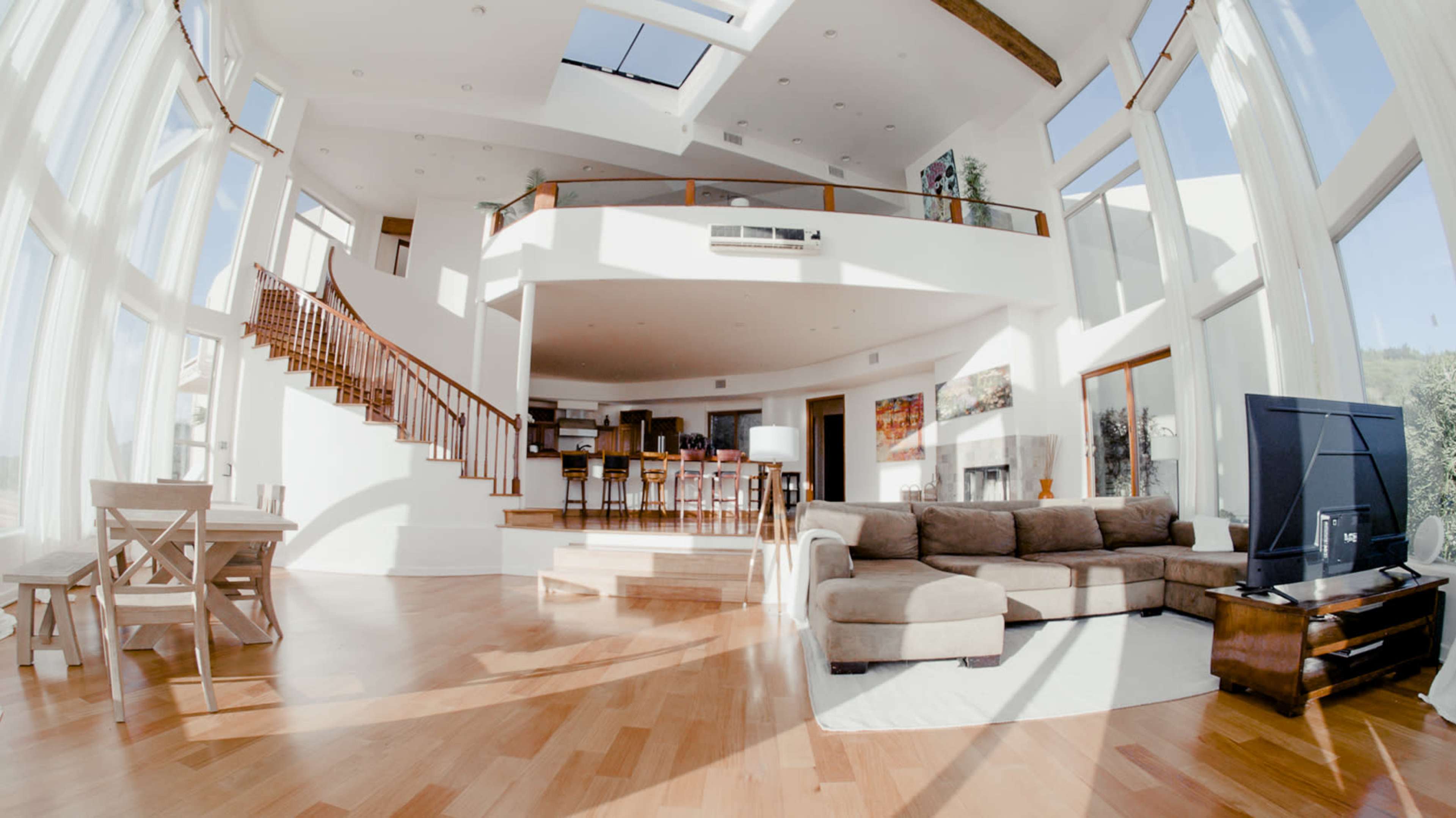 A spacious living room with large windows, a staircase leading to an upper level, and a sectional sofa facing a television.
