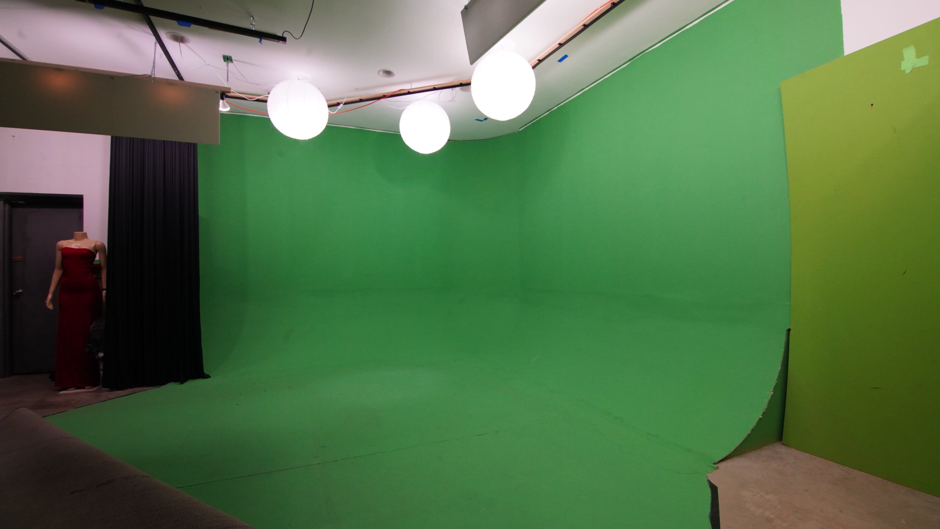 The image shows a green-screen studio with a seamless green backdrop and three hanging round lights.