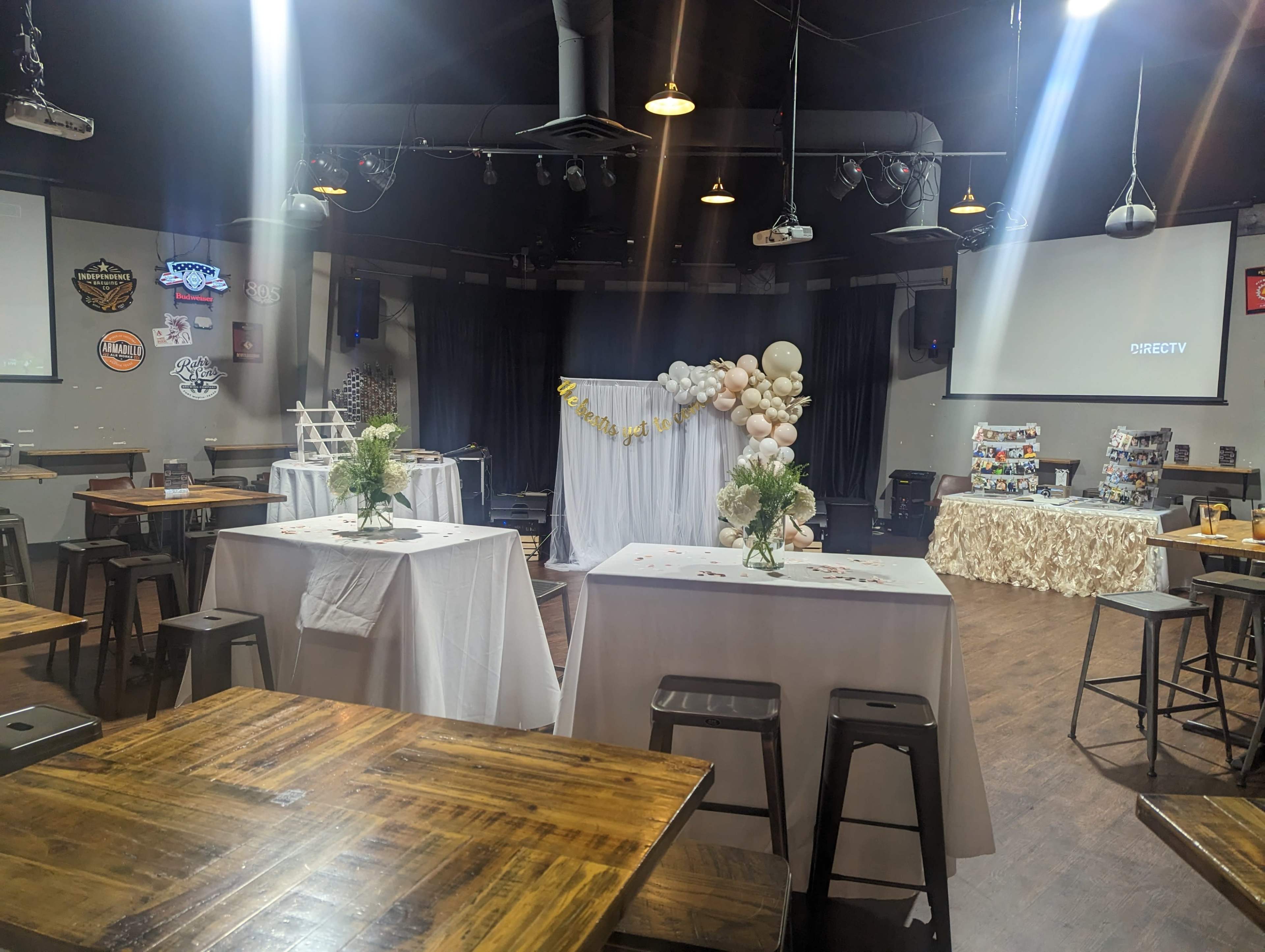 A decorated event space with tables set for a celebration, featuring a backdrop of balloons and floral arrangements.