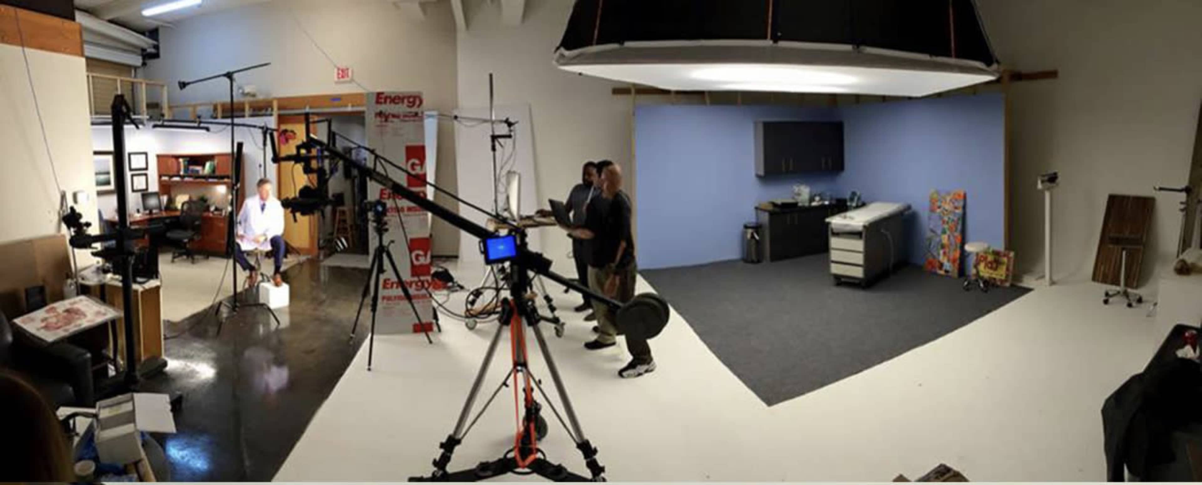 A video production studio with various lighting and camera equipment, a blue backdrop, and a kitchen setup.
