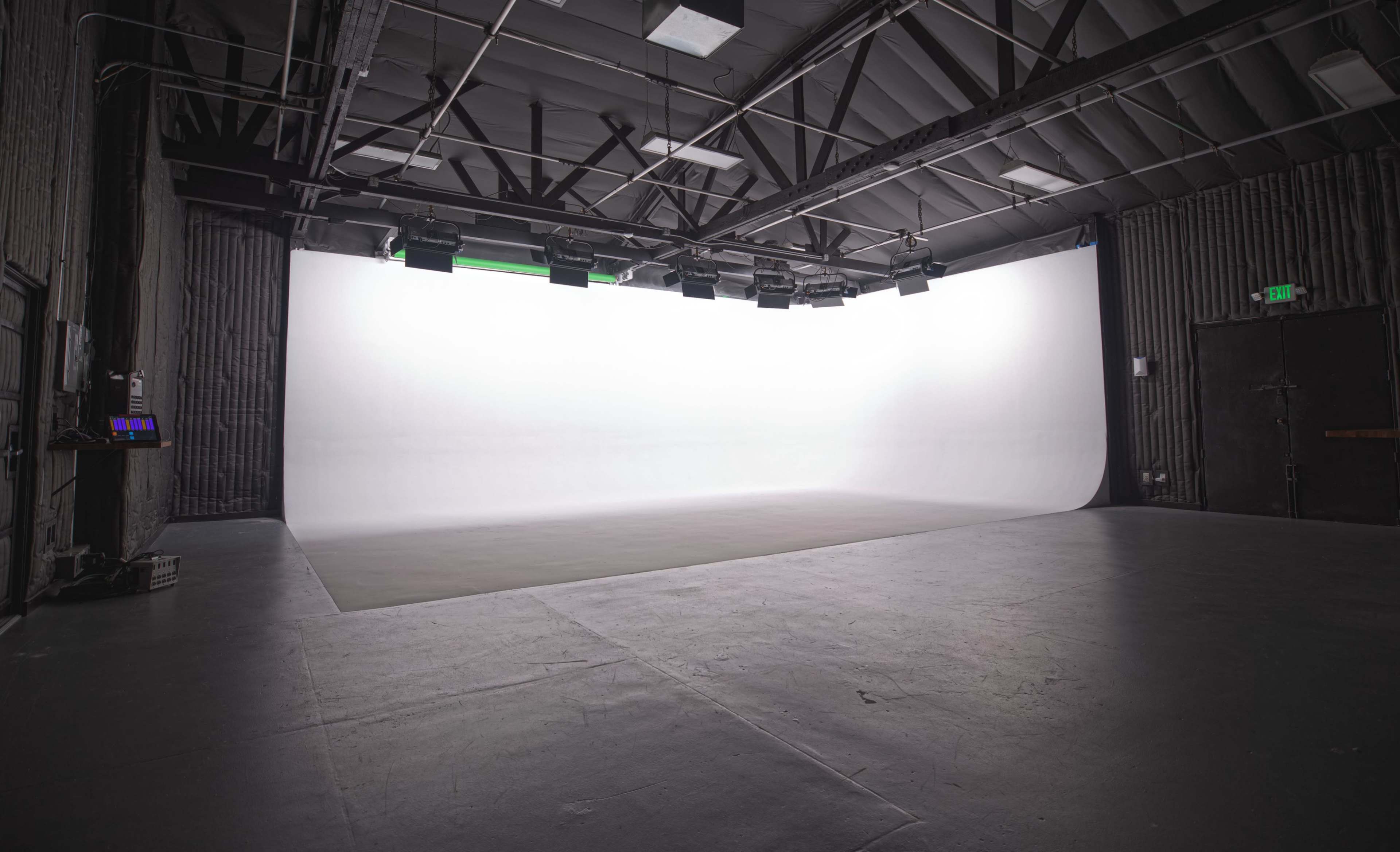 The image shows a spacious studio with a seamless white backdrop and a smooth gray floor, illuminated by overhead lights.